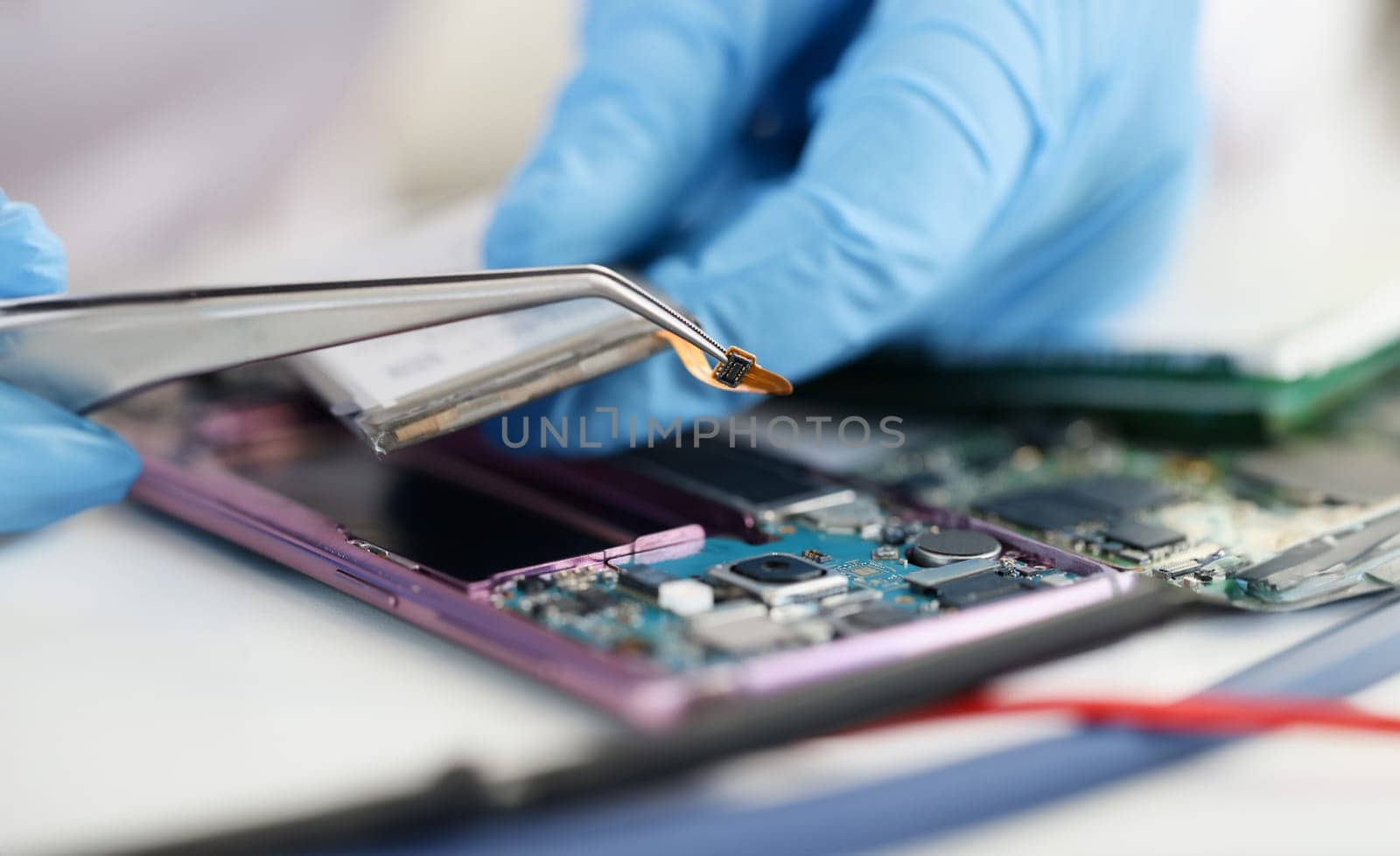 Master in rubber gloves holding microchip over broken phone in workshop. Mobile phone repair concept