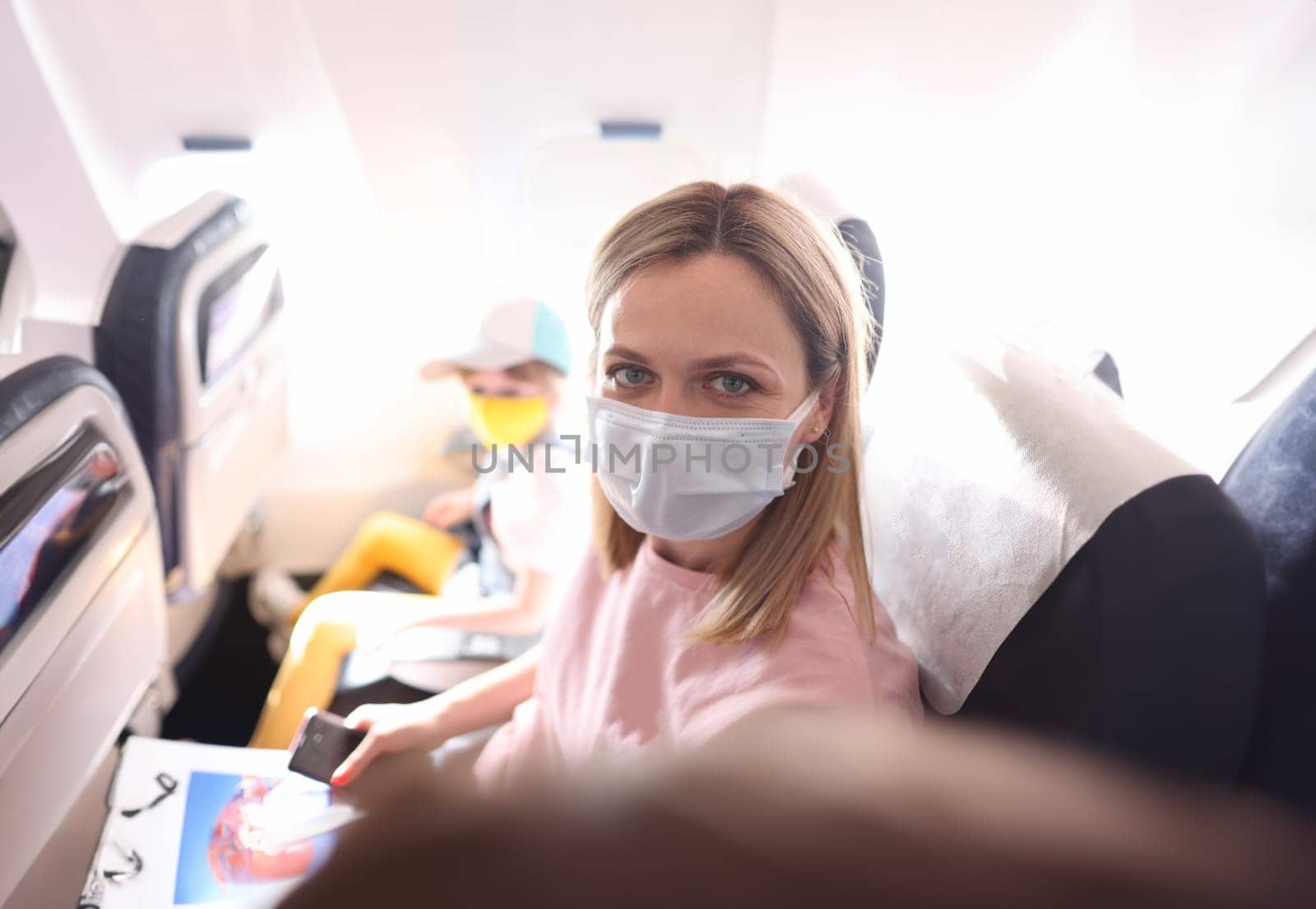Young woman in protective mask making selfie in cabin of plane. Flight rules for passengers during covid19 pandemic concept