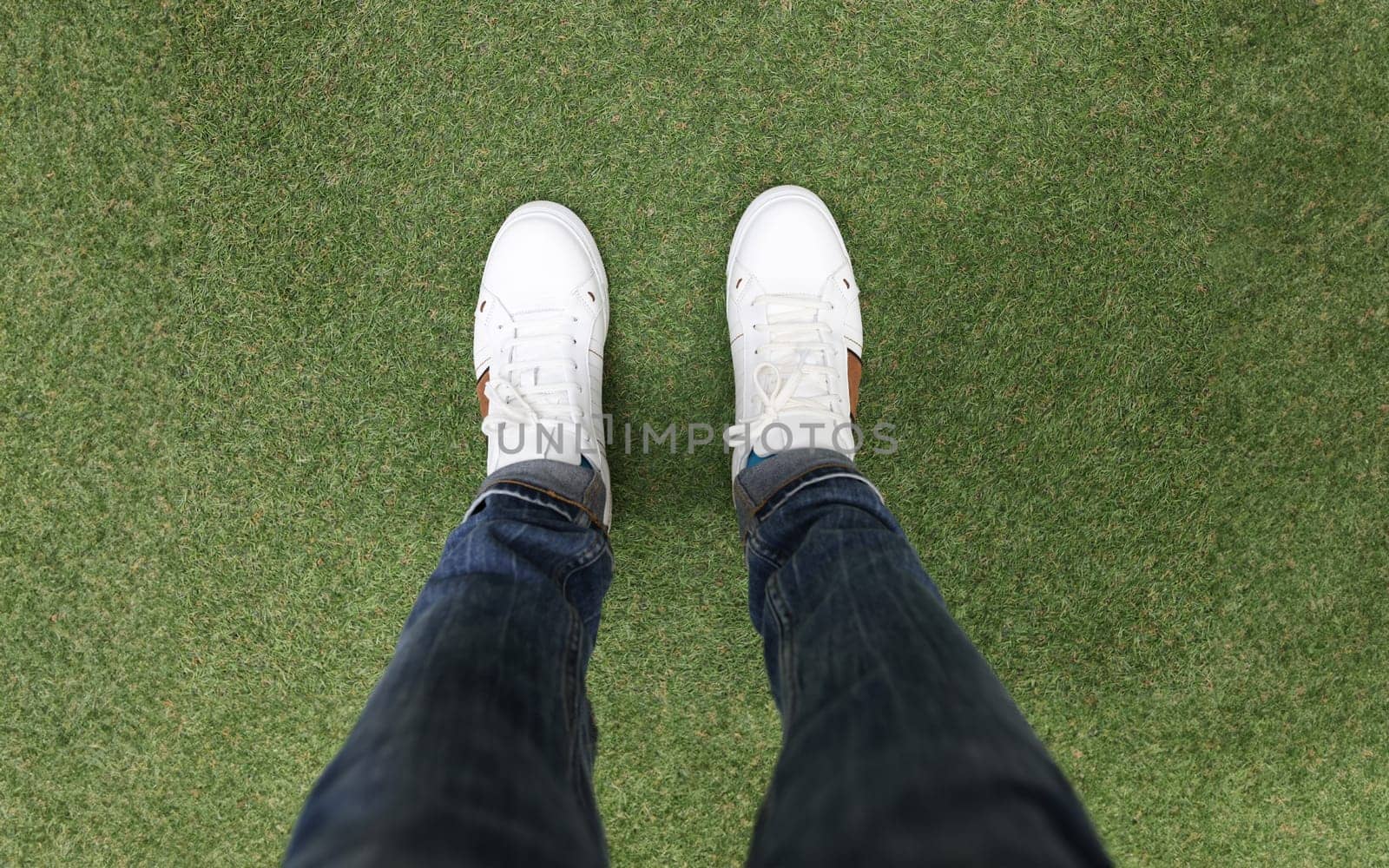 Male feet in white sneakers standing on green grass closeup. Walking in comfortable shoes concept