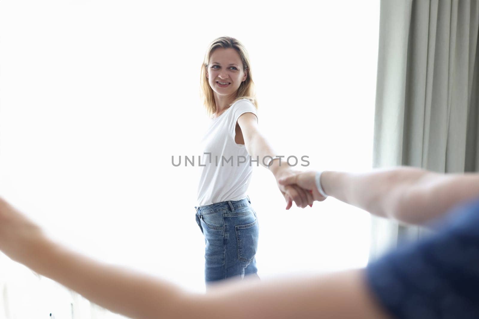 Young woman holding man hand near window at home. Romantic relationship concept