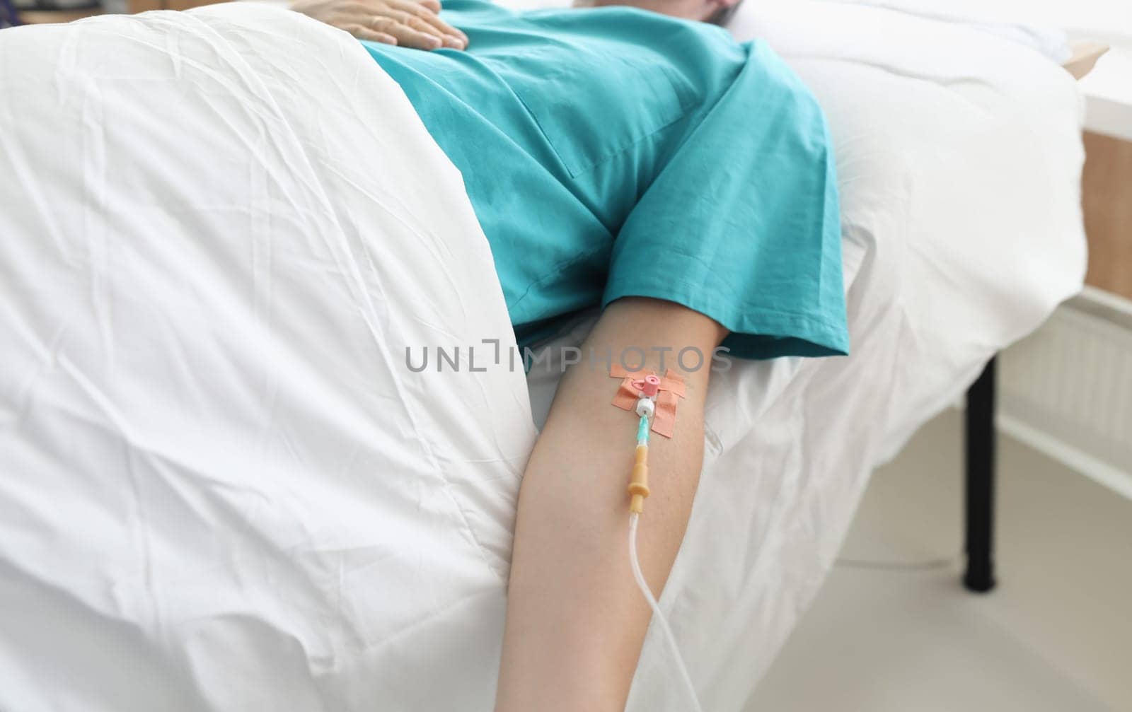 Man lies in hospital with syringe in vein his arm. Treatment an addict in hospital. Needle is fixed with patch to skin in direction vein. Treatment in clinic by administering an intravenous drug
