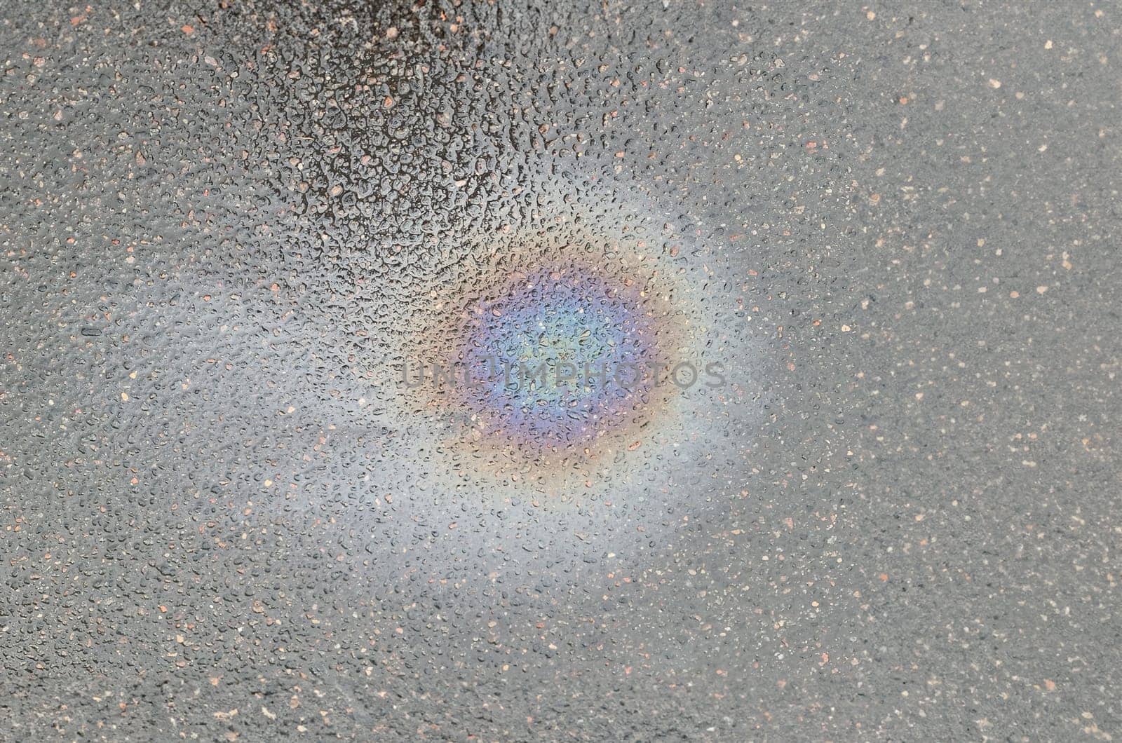 Bright rainbow spot on wet asphalt from gasoline closeup background. Technological disaster concept