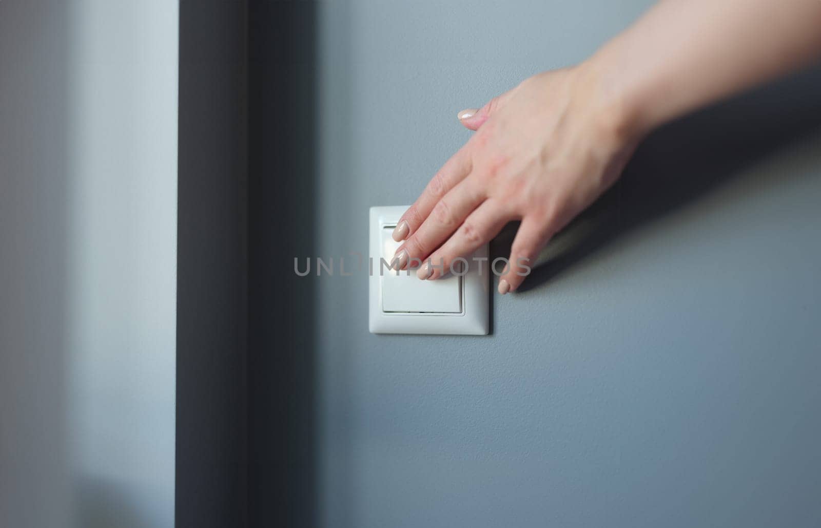 Female hand pressing light switch in apartment closeup. Energy savings concept