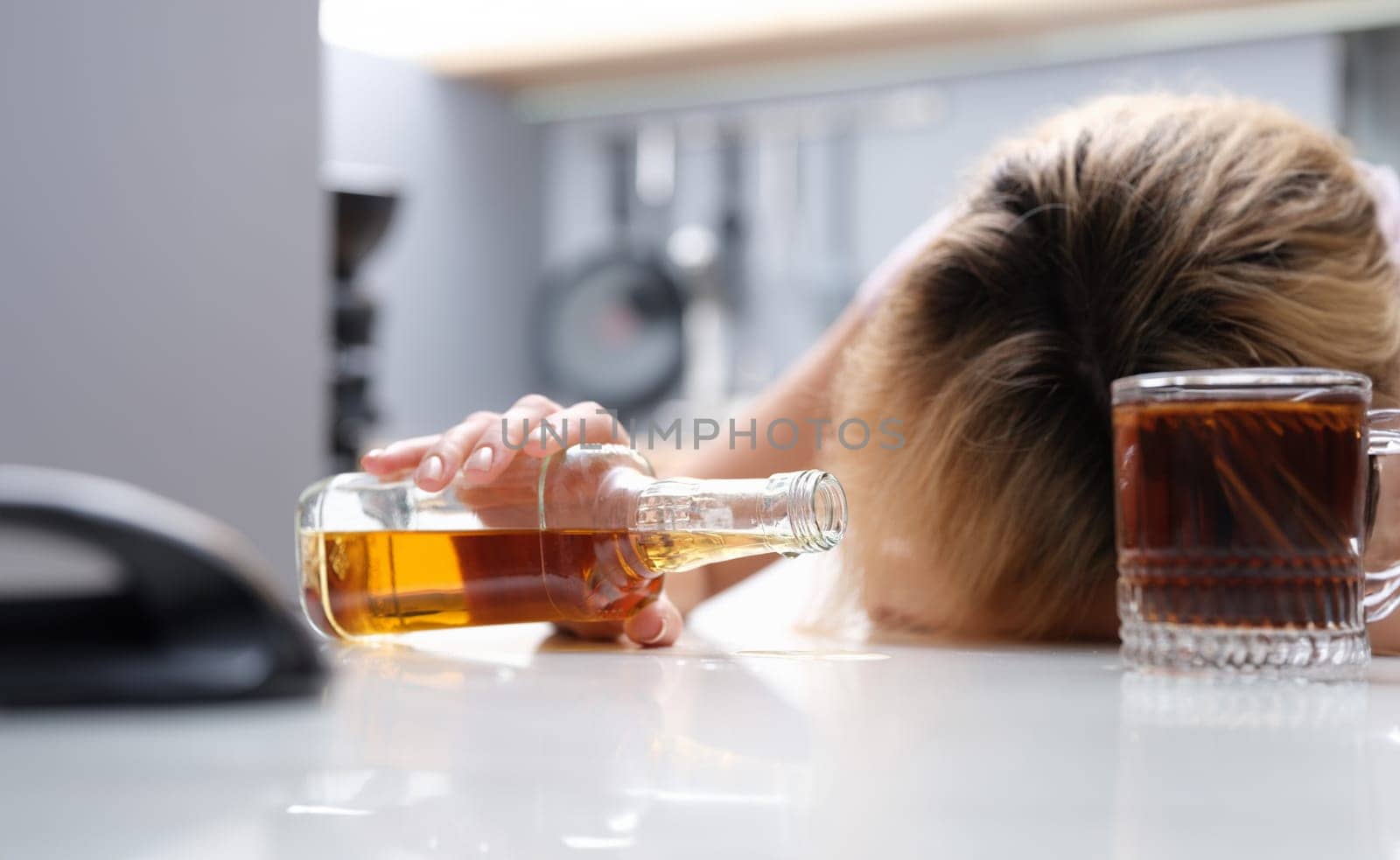 Woman sleeping at table with bottle of alcohol in her hands closeup. Alcohol addiction in women concept