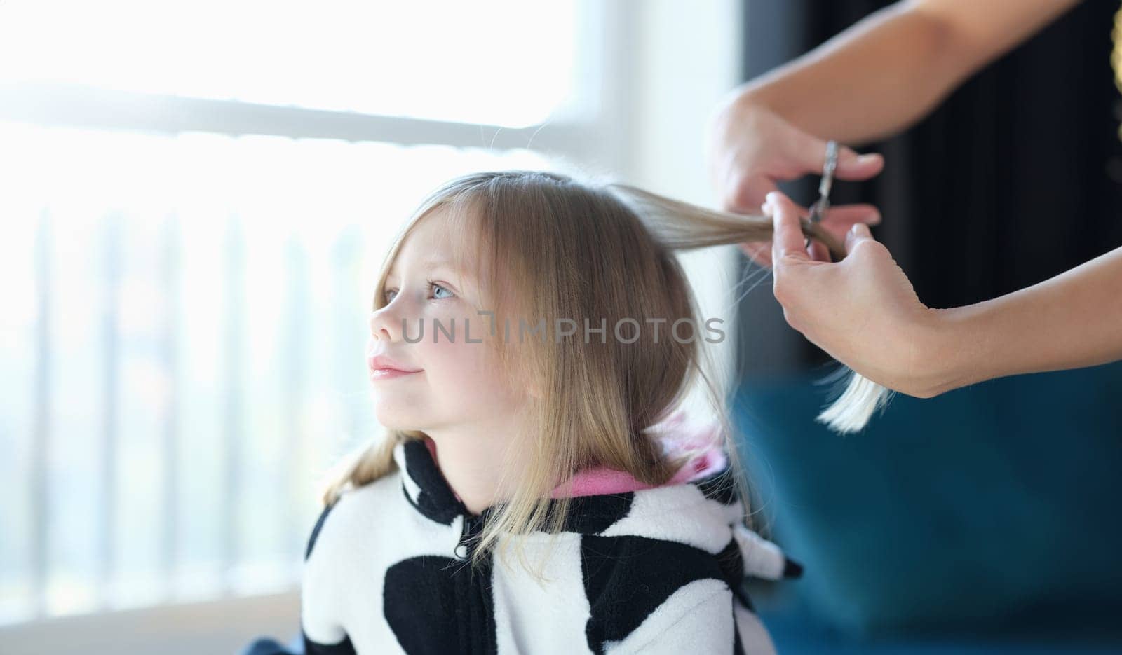 Hairdresser cutting hair of little girl in beauty salon. Hairdressing services for children concept