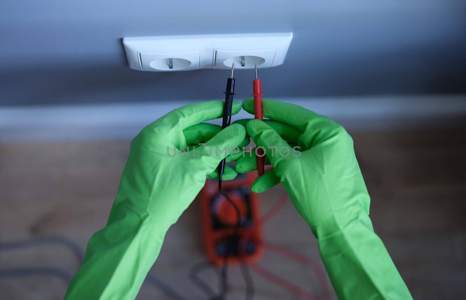 Craftsman in rubber gloves holding tester near electrical outlet at home closeup. Safety when working with electricity concept