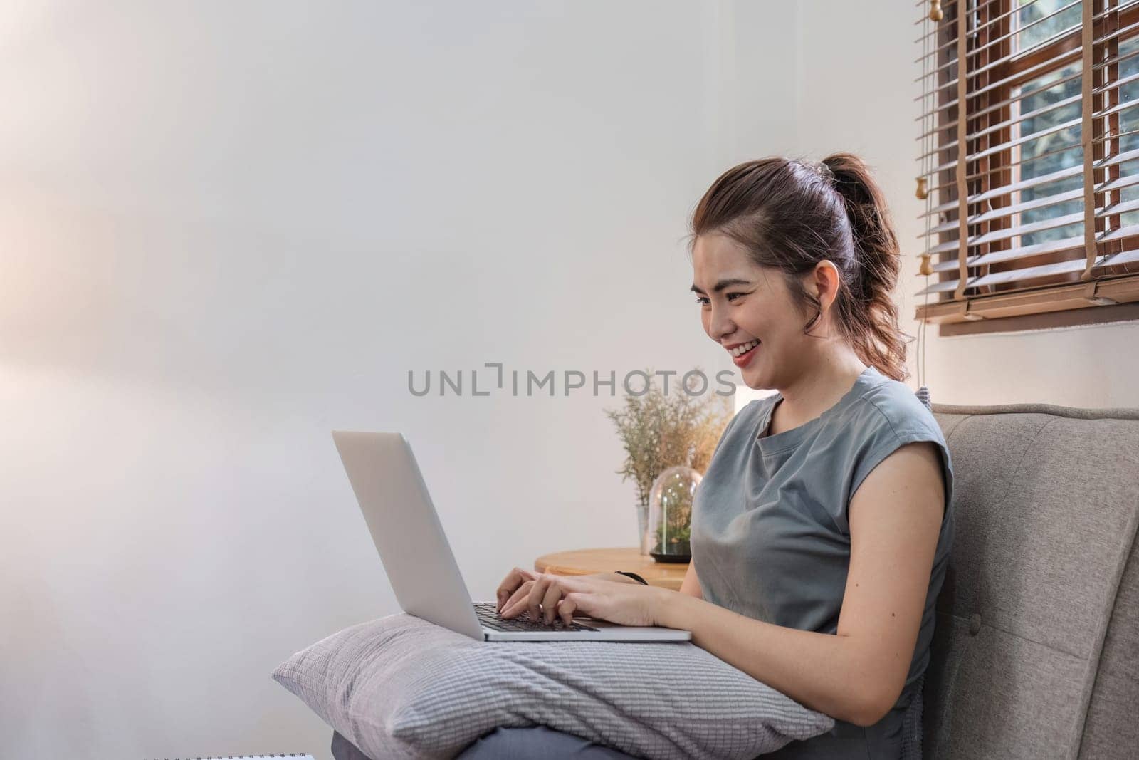 Young woman opens laptop Start working in education, sending messages, shopping online. Watch a movie in the living room at home. Portrait of a girl sitting on a sofa. Lifestyles.