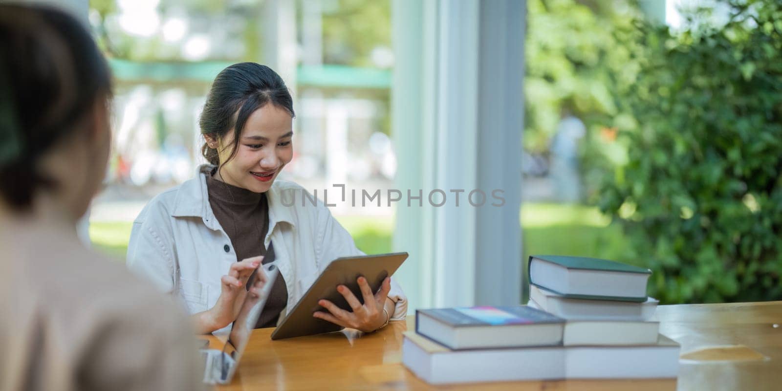 University students sitting together at table with book and laptop. Happy young people doing group study in college campus.