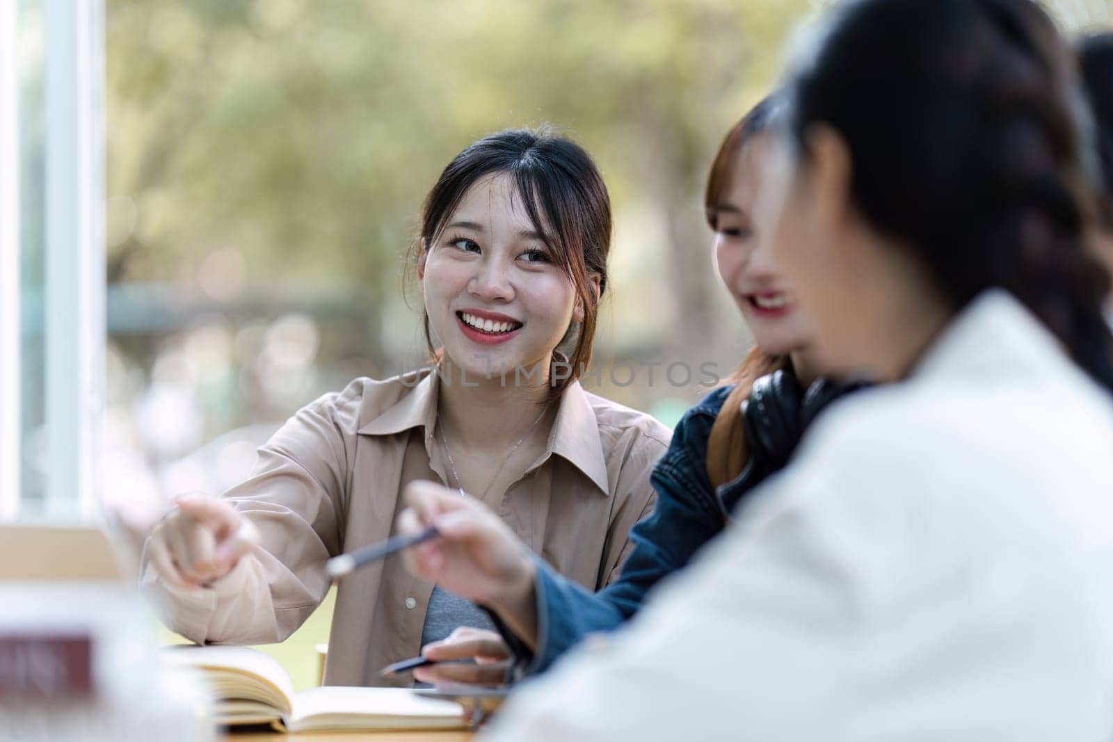 Group of young Asian college students sitting on a bench in a campus relaxation area, talking, sharing ideas, doing homework or tutoring for the exam together by itchaznong