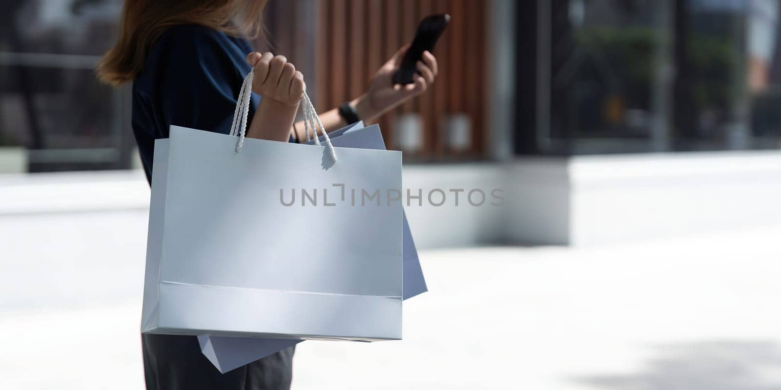 Woman using smartphone holding Black Friday shopping bag while standing on the stairs with the mall background by nateemee