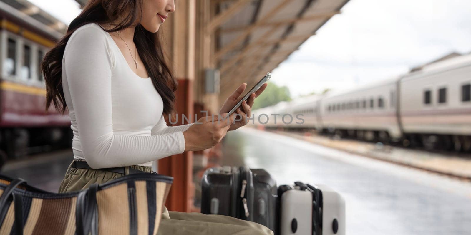 Asian female traveler using her smart phone mobile while waiting for a train at a station.