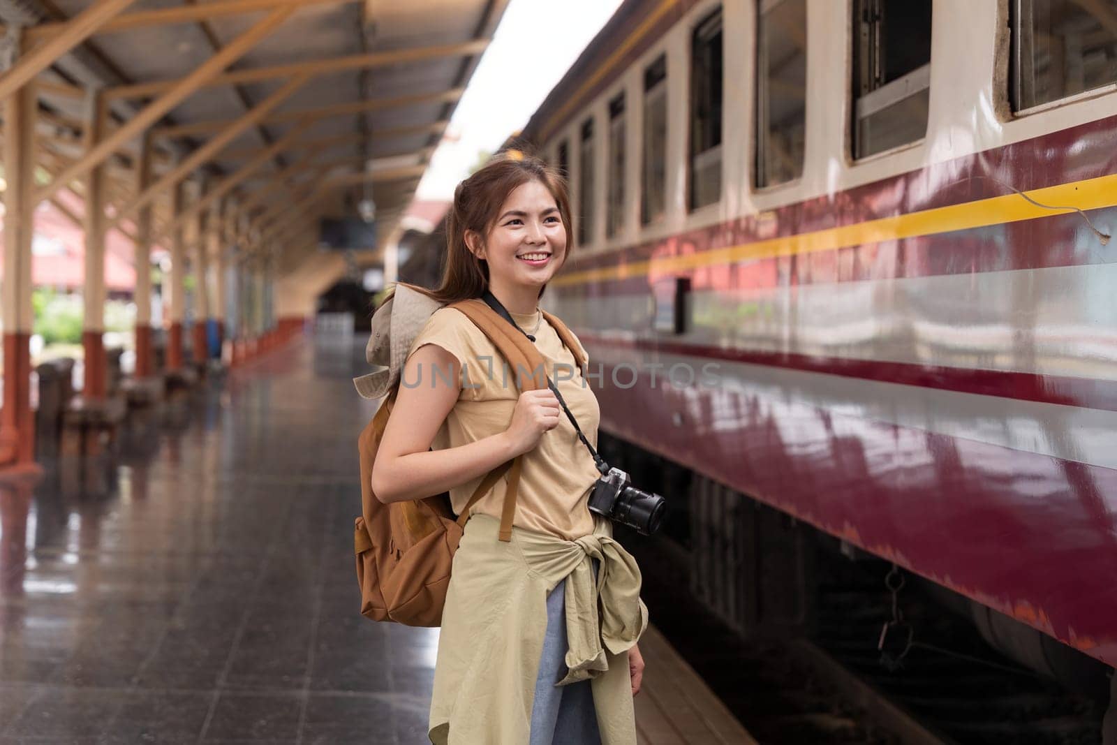 Beautiful asian traveler with backpack getting on a train at a platform of railway station.