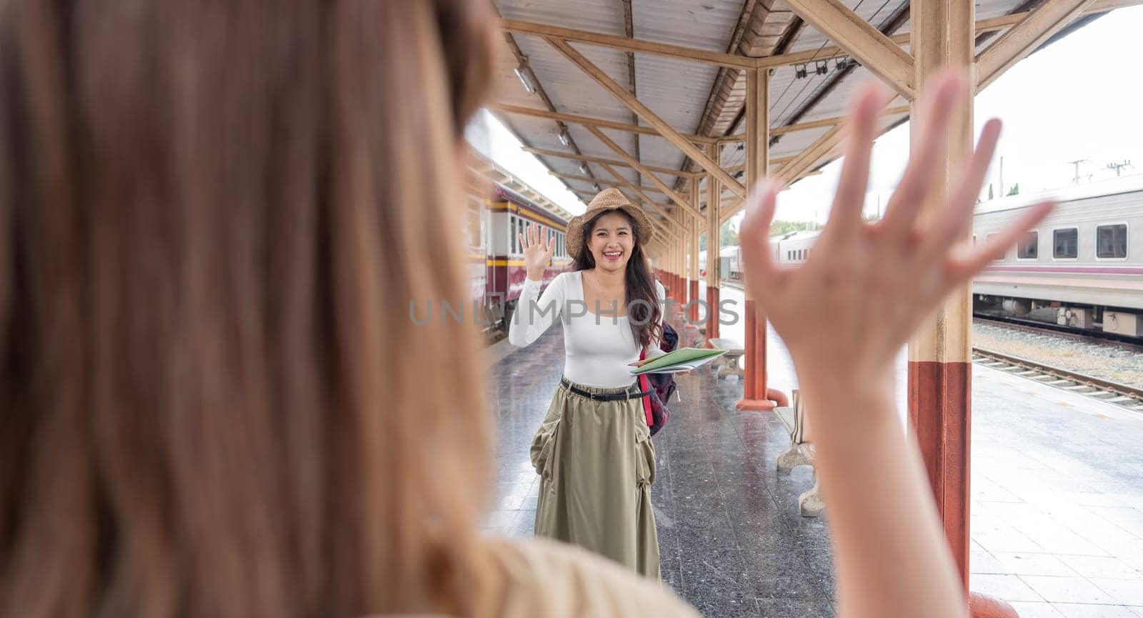 Asian female tourist waves greet to friend who are going on a trip at the train station.