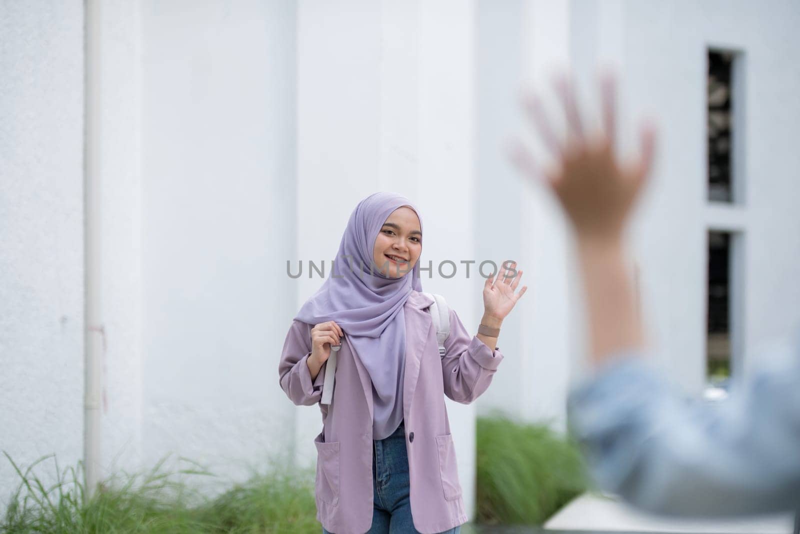 Beautiful Muslim college student girl waving to greet a friend at university.