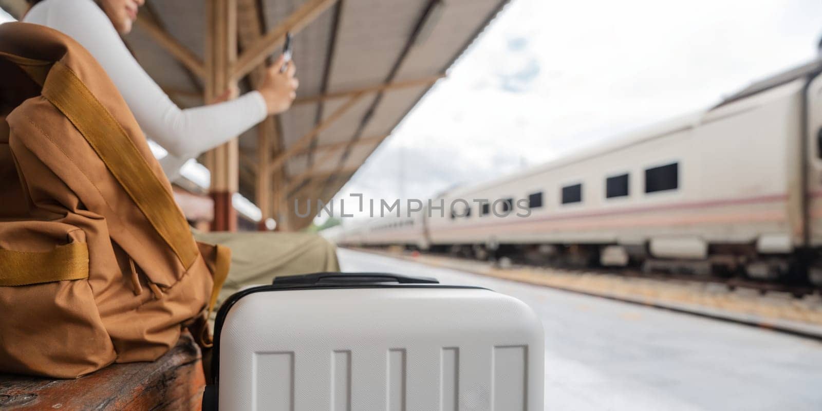 Asian female traveler using her smart phone mobile while waiting for a train at a station by nateemee