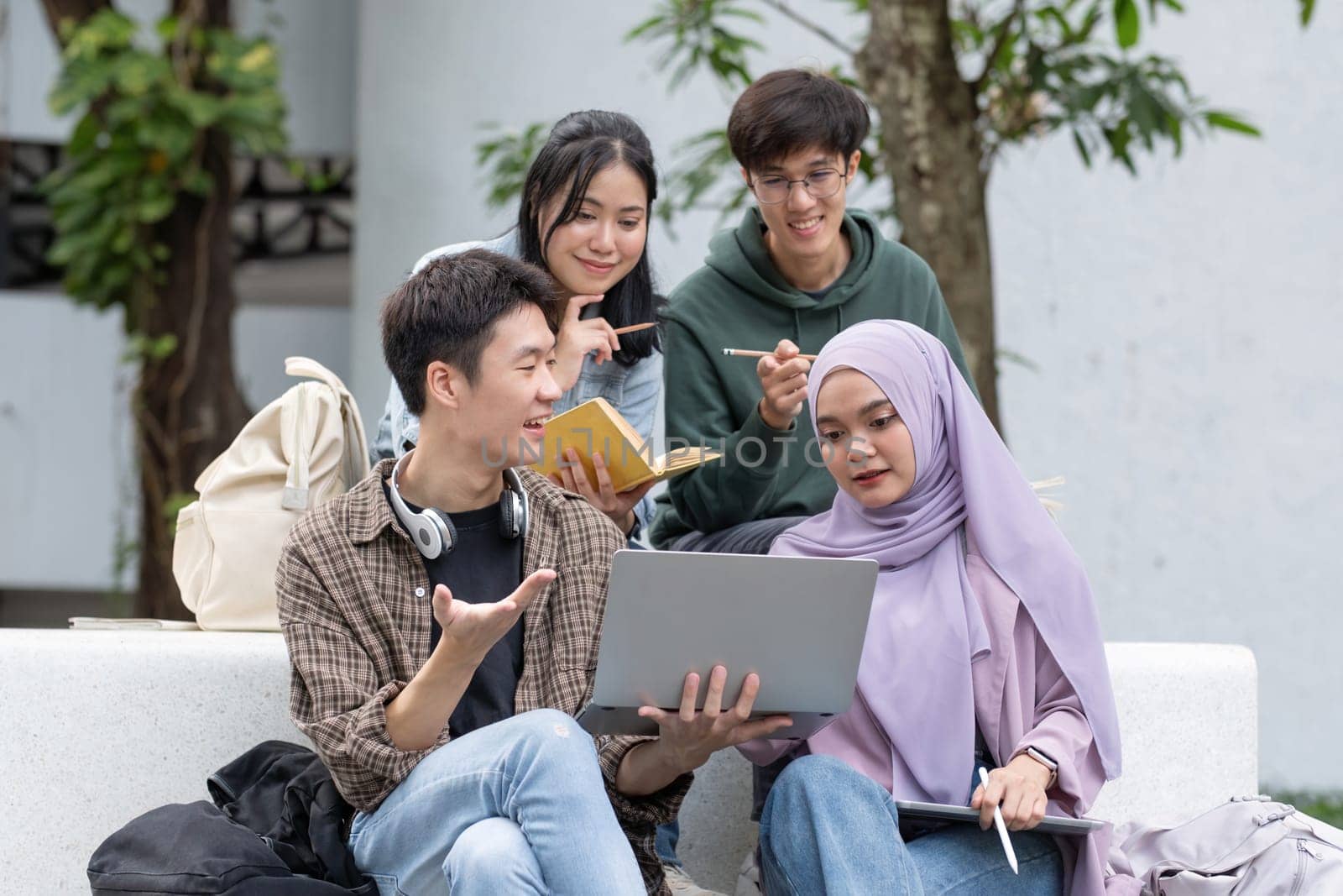 Multiracial smiling group of teenage student using laptop doing homework and enjoying a relaxed atmosphere outdoors at the university campus. Education concept. High quality photo.