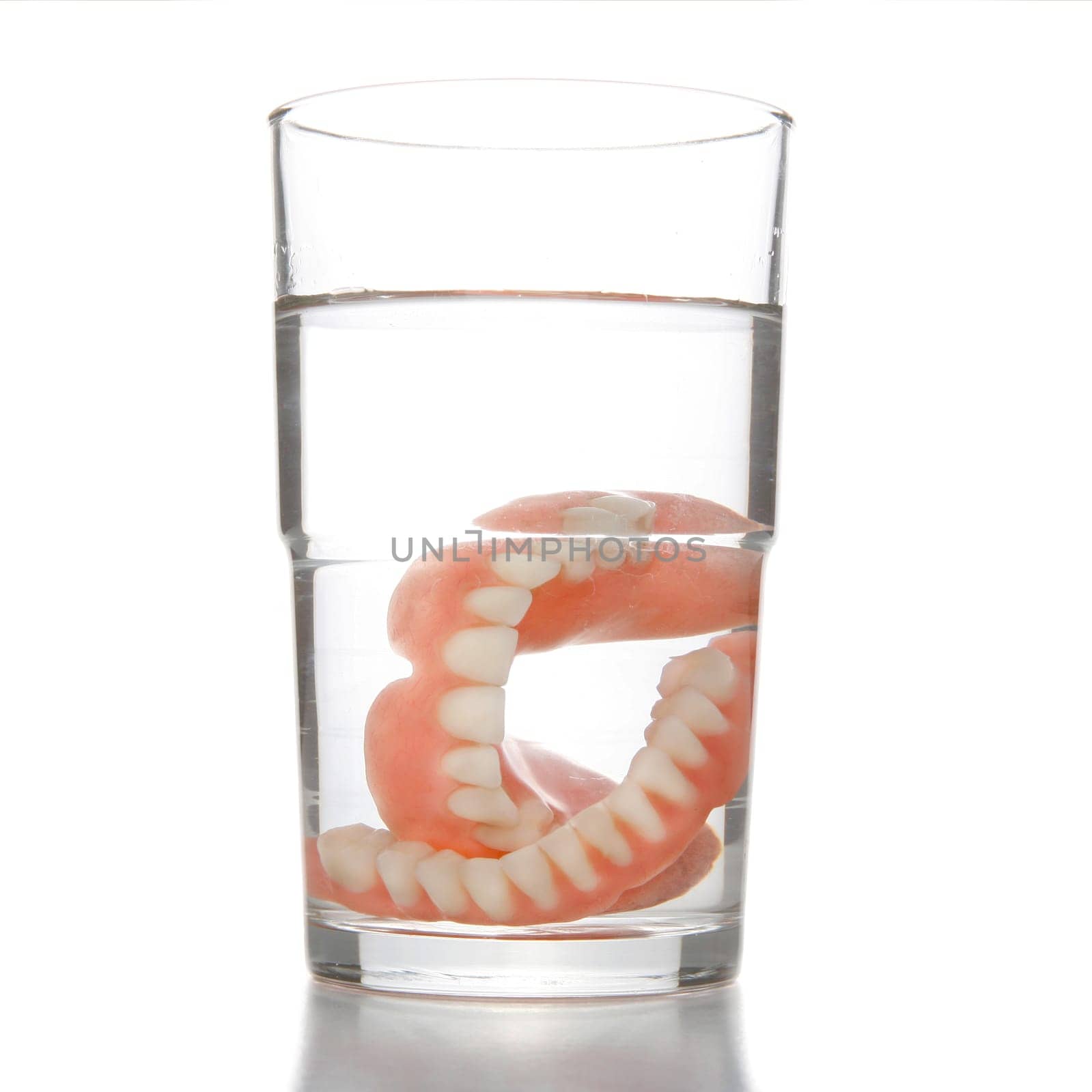 False teeth having a swim in transparent water glass