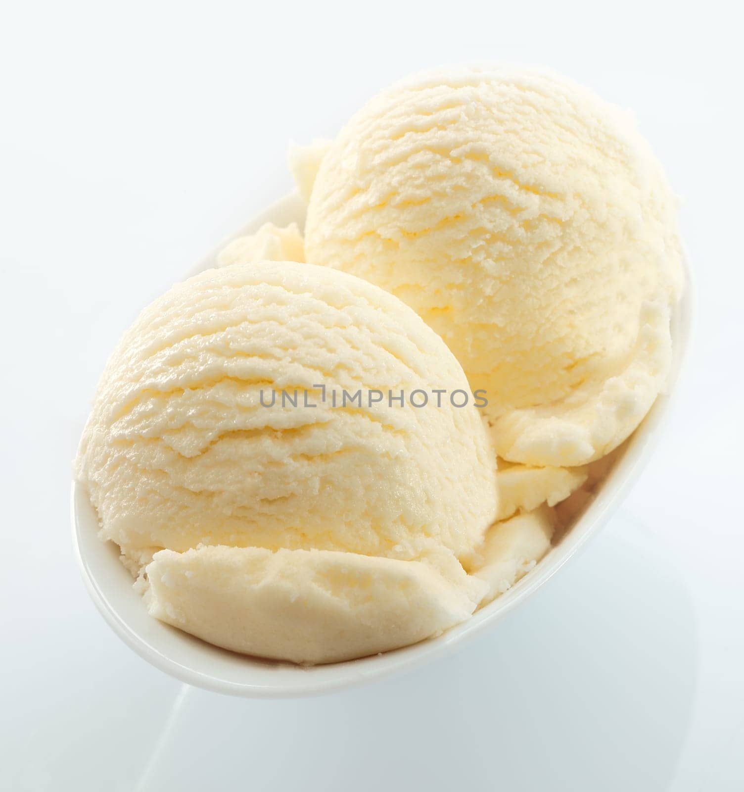 High angle view of scoops of creamy vanilla icecream served in a small white dish on a white background
