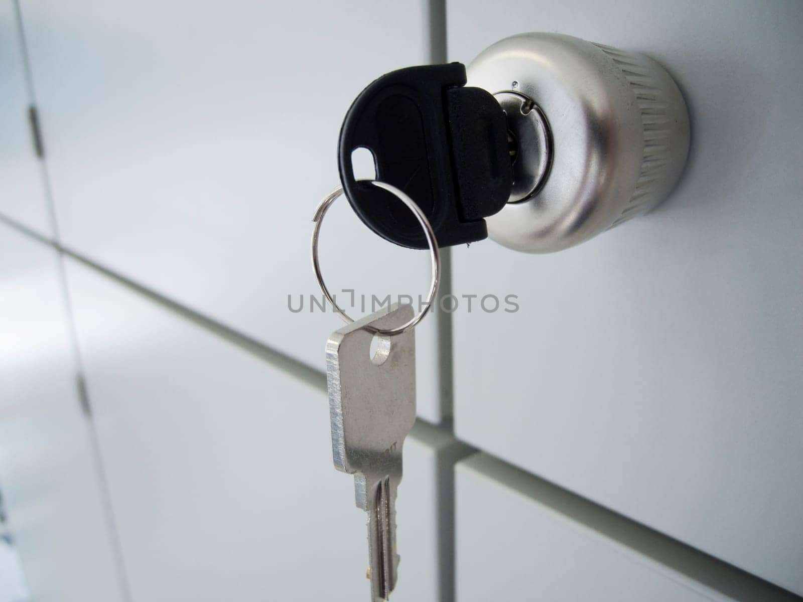 Close-up of a gray cabinet door with a round handle and inserted and hanging keys,as well as intersecting spacer gaps in oblique view
