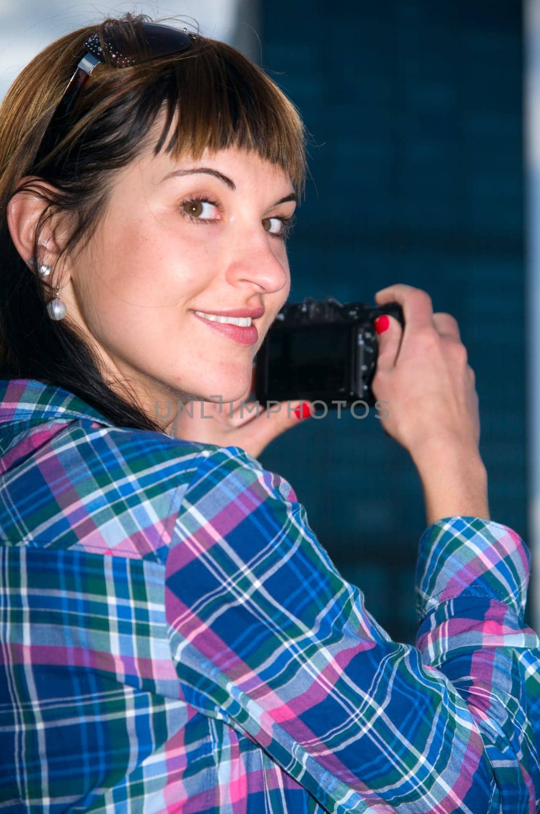 Exterior shot of young brunette woman wearing sunglasses and camera in side view and looking at camera