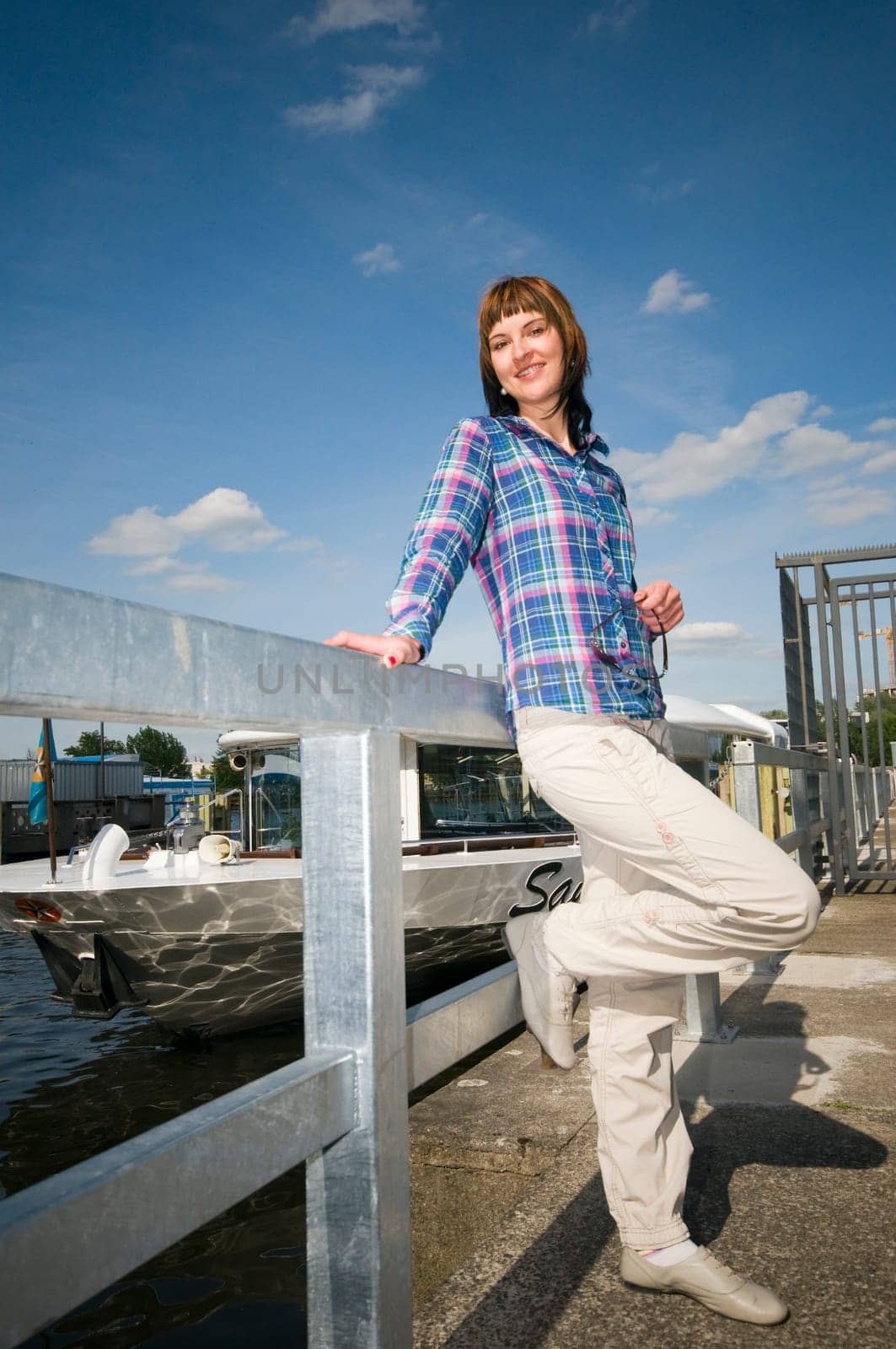 Full length portrait of a young brunette woman leaning on a railing and excursion steamers in blurred background