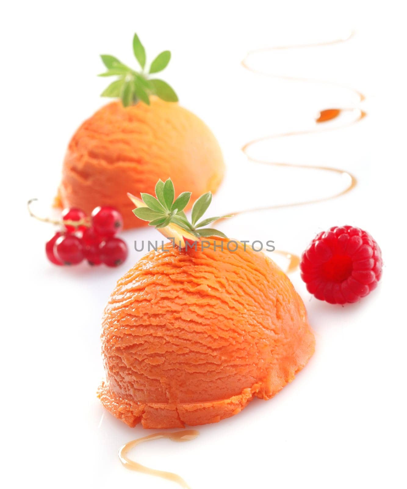 Balls of exotic tropical mango ice-cream garnished with berries on a white studio background