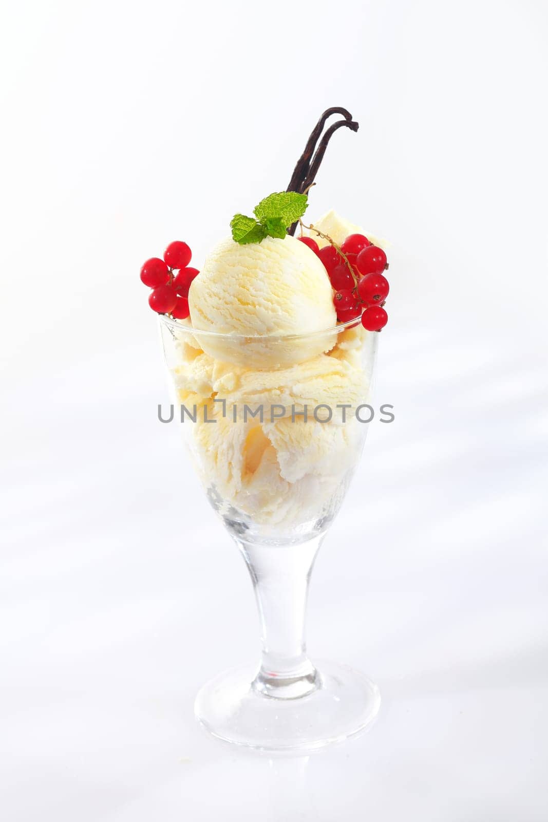 Serving of vanilla icream with colourful ripe redcurrants in a glass container garnished with dried vanilla pods