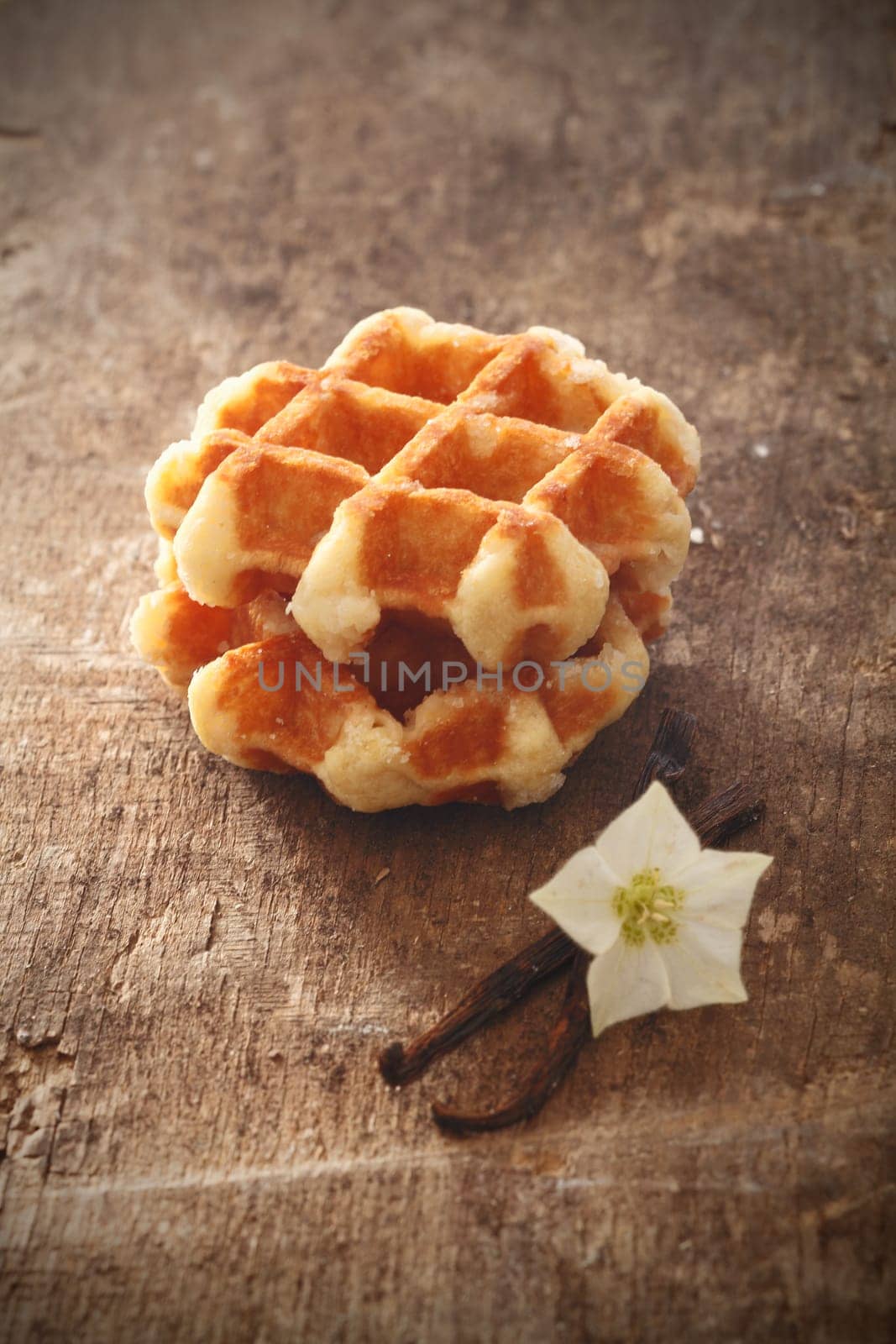 Freshly baked crisp golden waffles on on old wooden table with vanilla pods and a flower