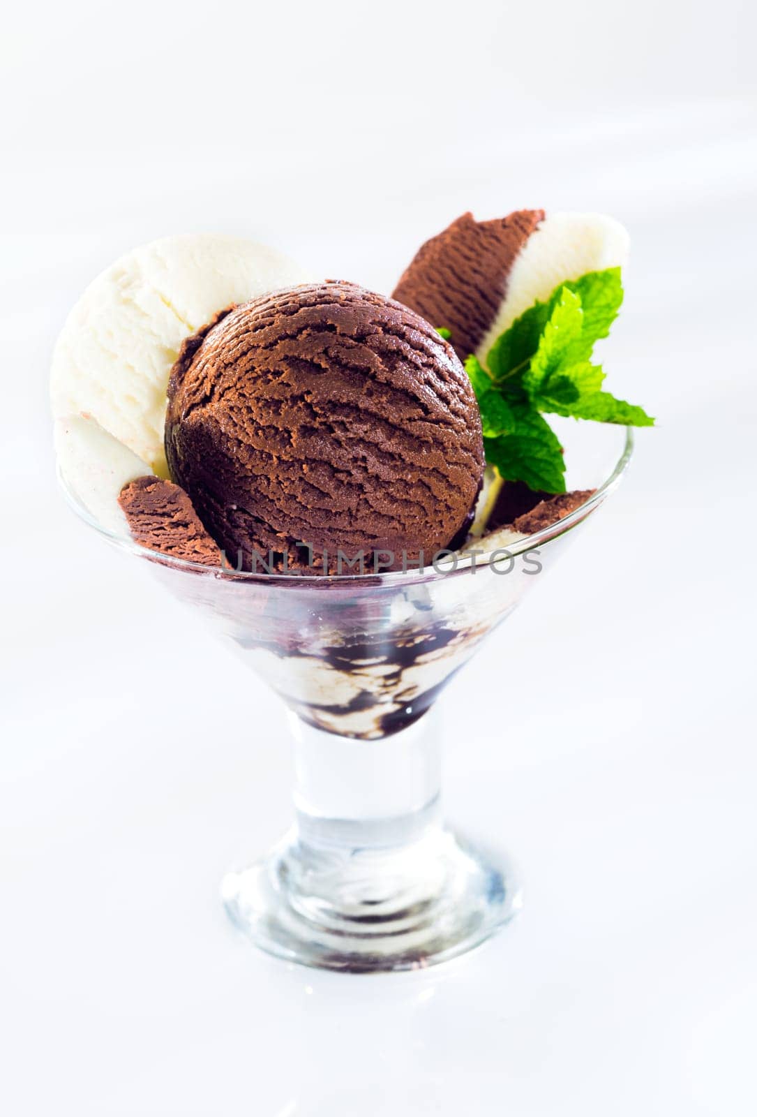 Glass cocktail glass filled with balls of textured creamy chocolate and vanilla ice cream garnished with mint