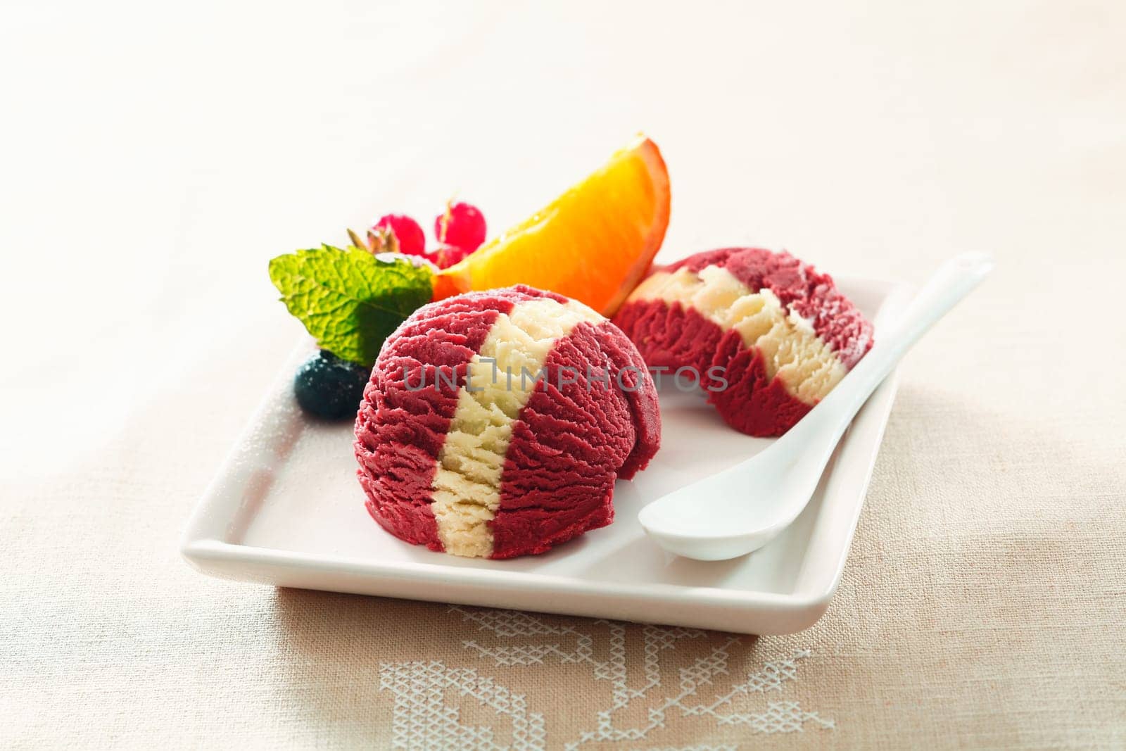 Serving of tropical berry ice-cream dessert with a colourful white stripe and fresh orange and redcurrant garnish