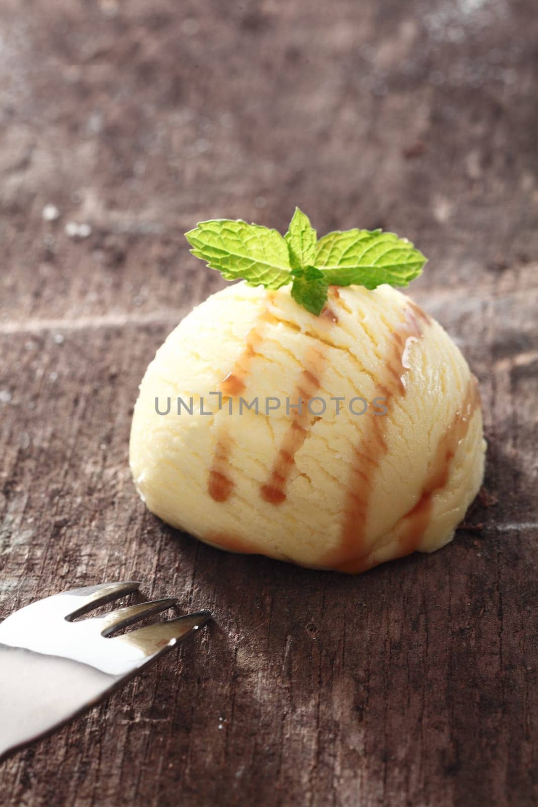 Single scoop of vanilla icecream drizzled with sauce on a textured old wooden table