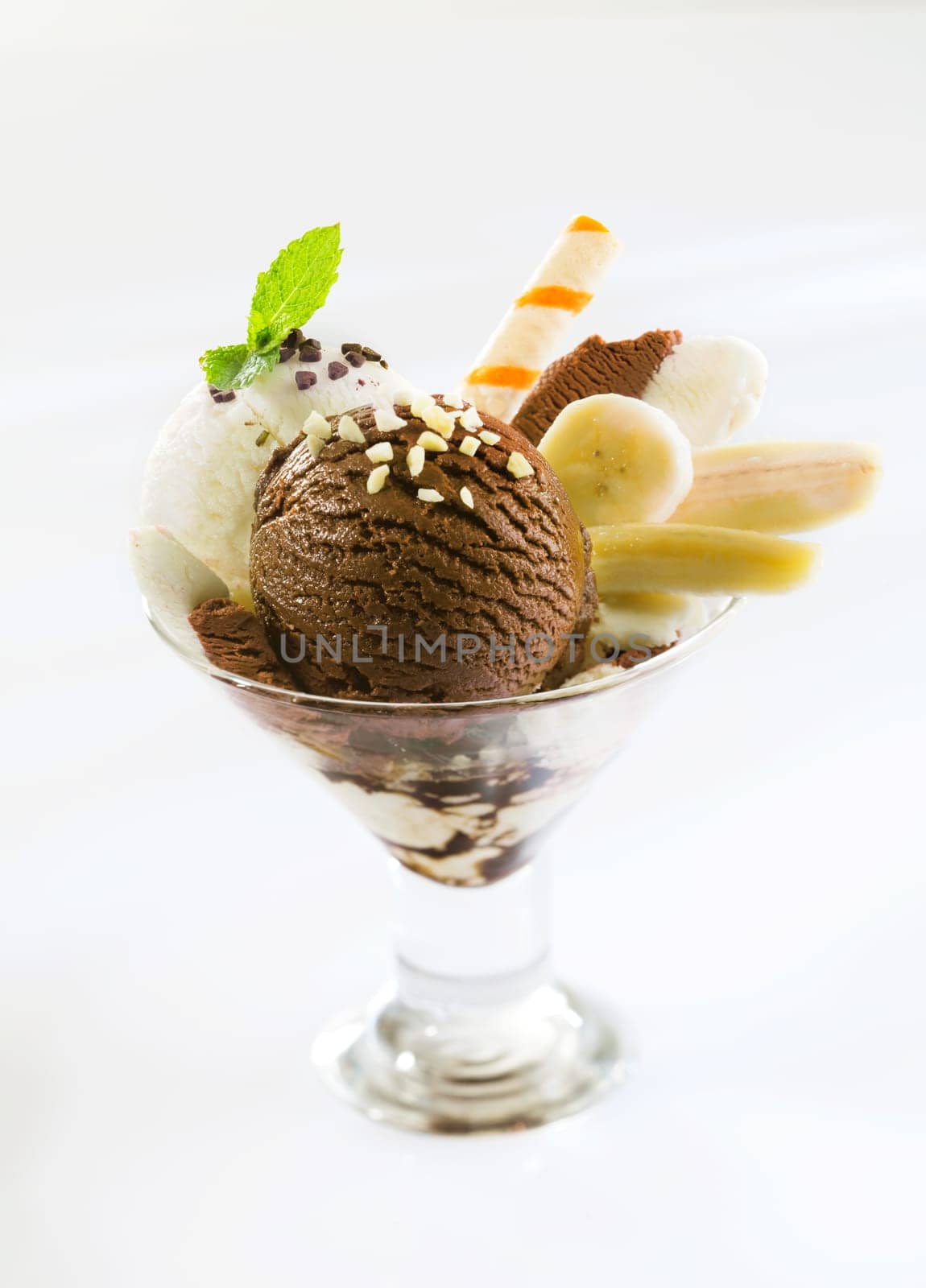 Fresh banana slices served with chocolate and vanilla icecream topped with nuts in a cocktail glass