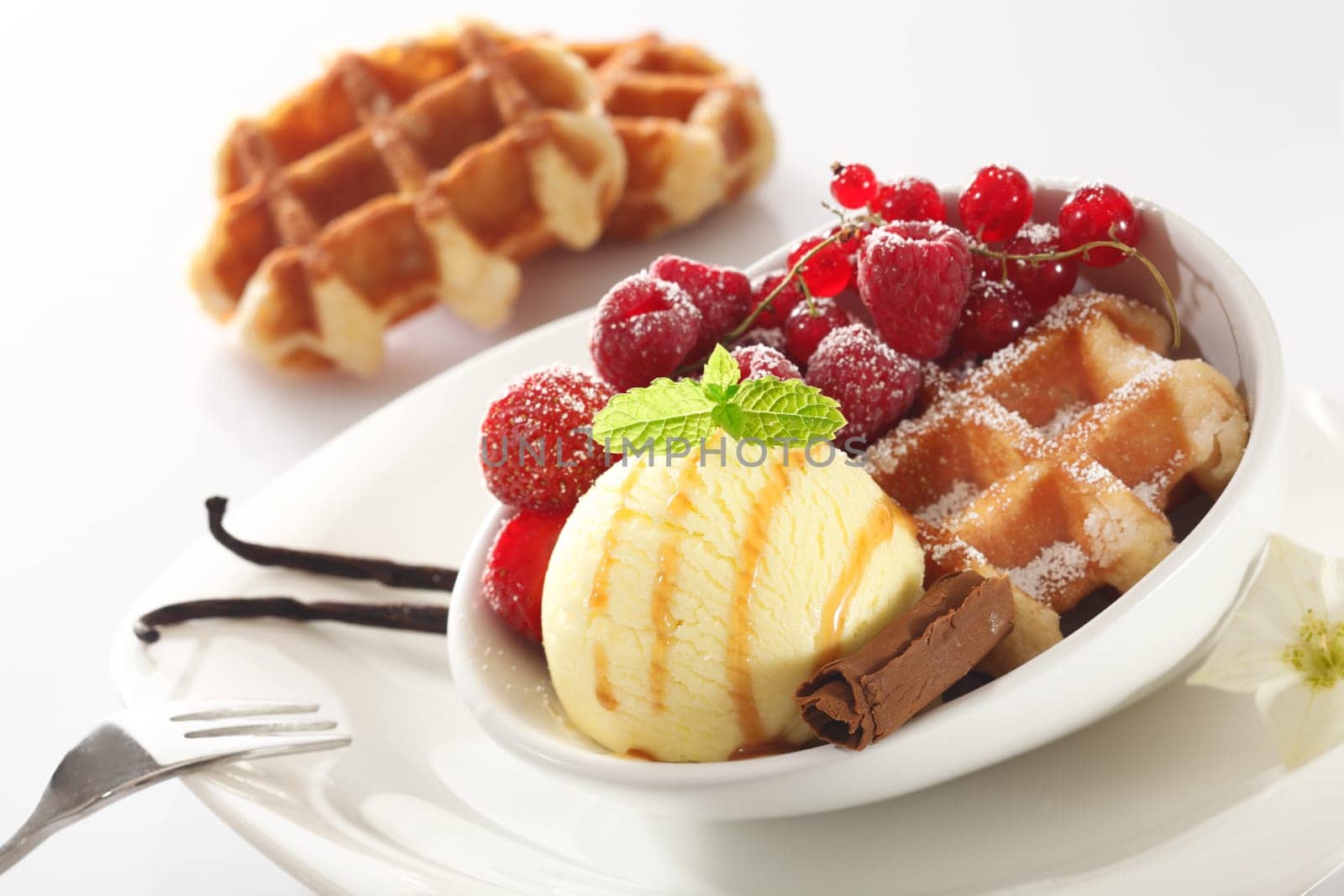 Tilted angle view of a healthy berry and icecream dessert with raspberries, strawberries and redcurrants on a crisp baked waffle