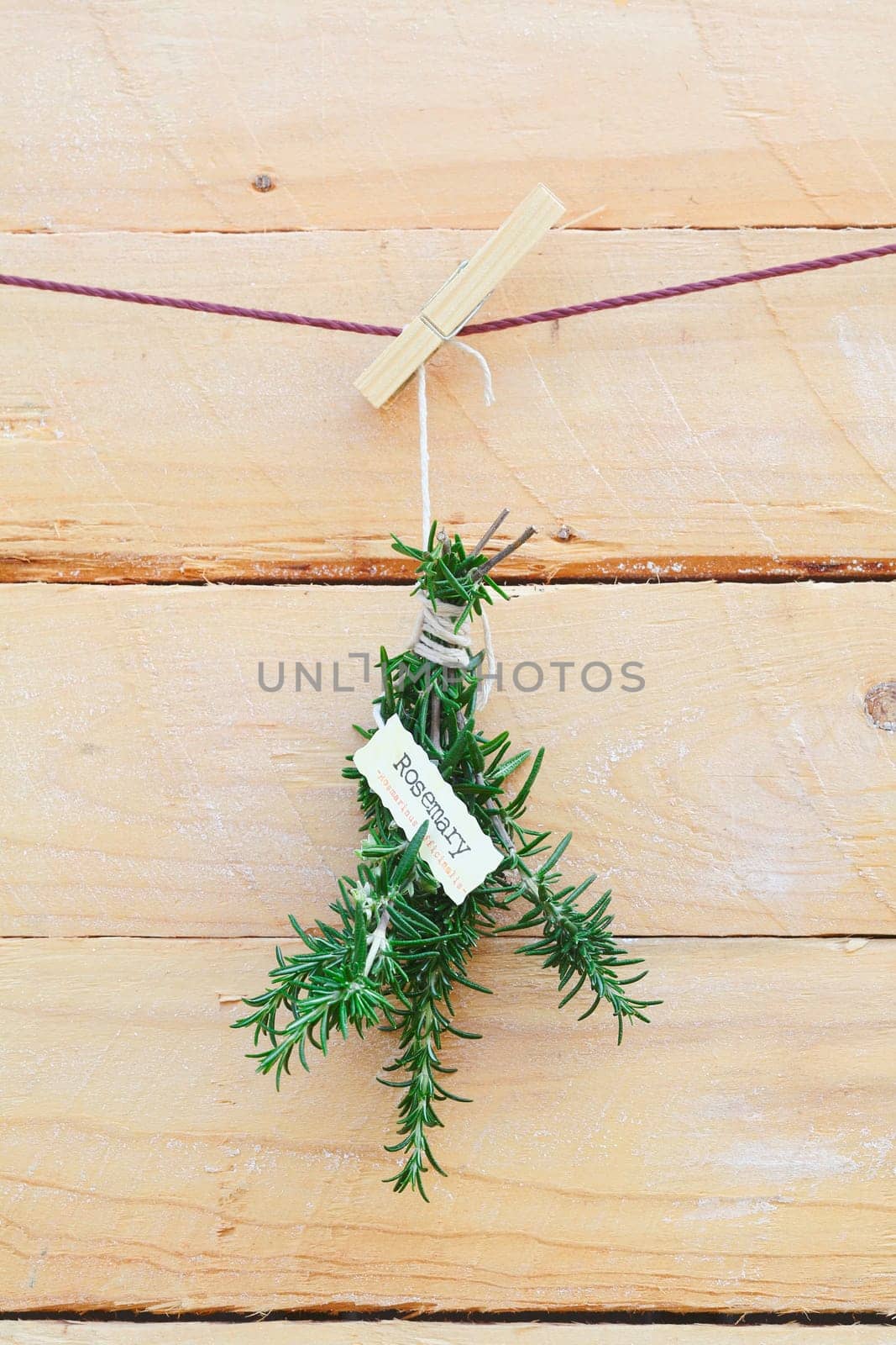 Fresh rosemary herb with a name label hanging from a clothespeg against wooden planks