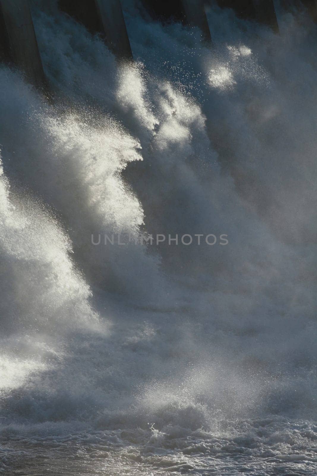 The sun dramatically backlighting the spillway of a large hydroelectric dam overflow.