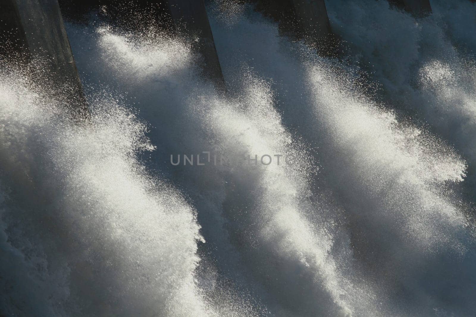 The sun dramatically backlighting the spillway of a large hydroelectric dam overflow.