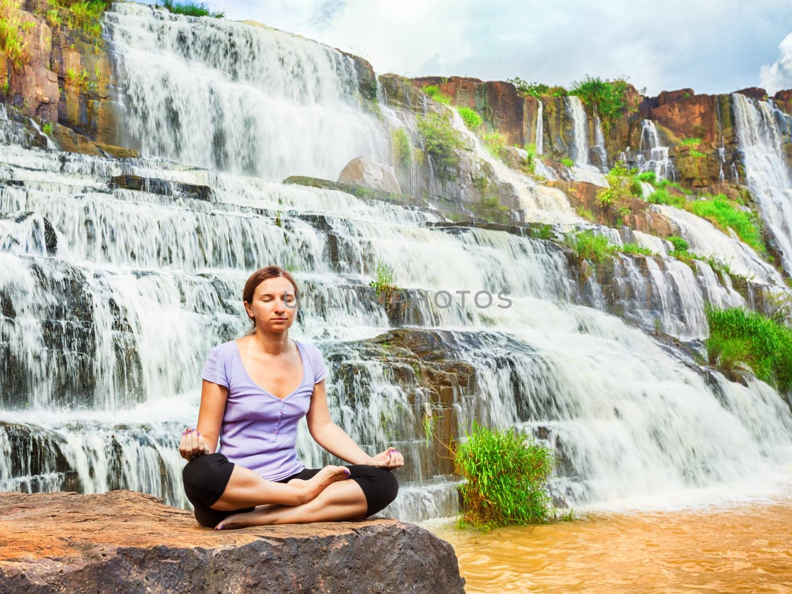 Beautiful woman meditating near waterfall