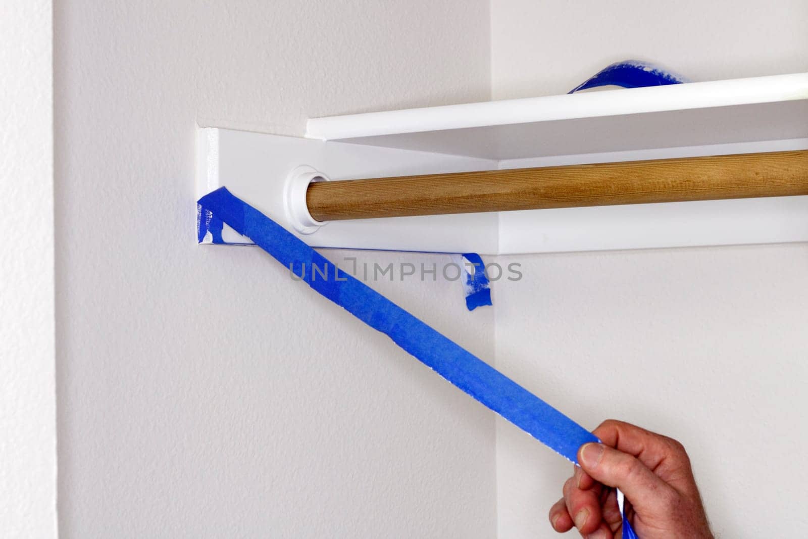 Blue painter&#039 s tape being pulled off of closet shelf bracket after painting the closet walls white.