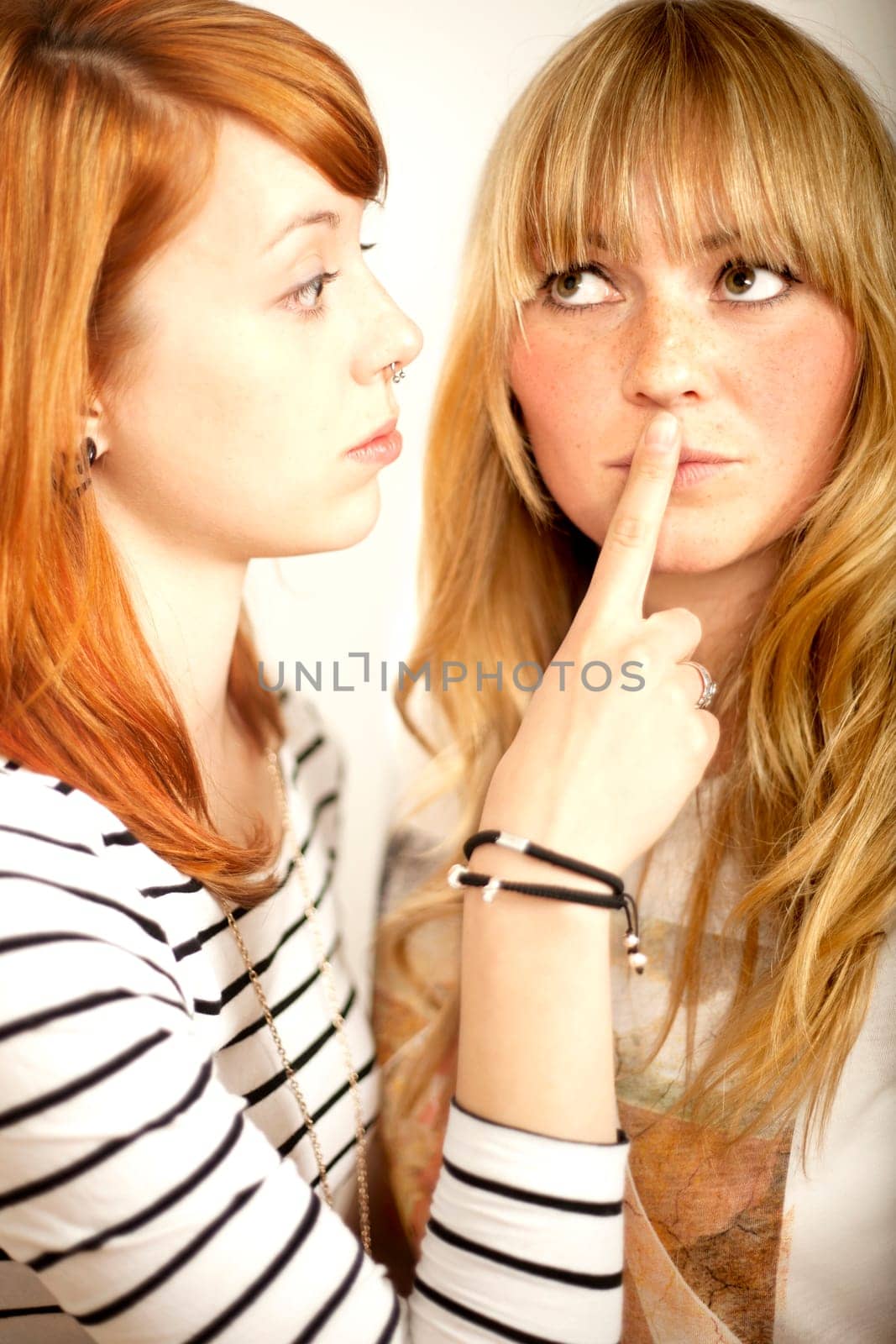 red haired and blond girl sign to shut up with finger