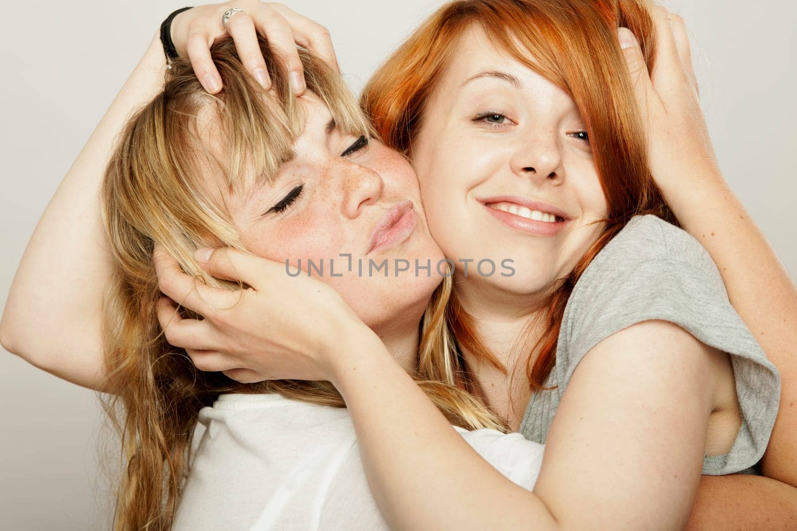 red and blond haired girls tousle hair with hands and smile