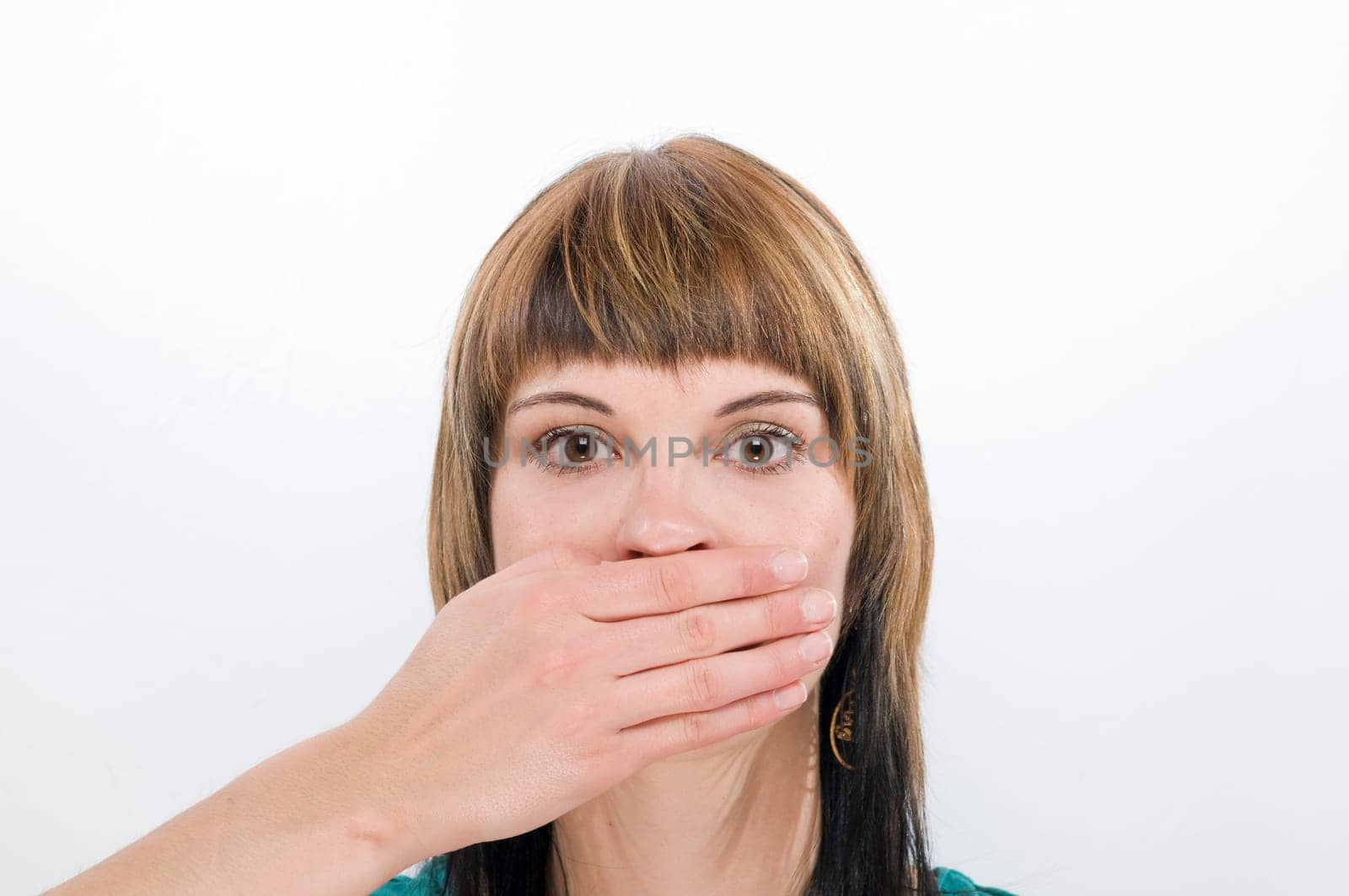 Head and shoulders view of a young woman looking at the camera and covering her mouth  Gesture: "don't say anything"""