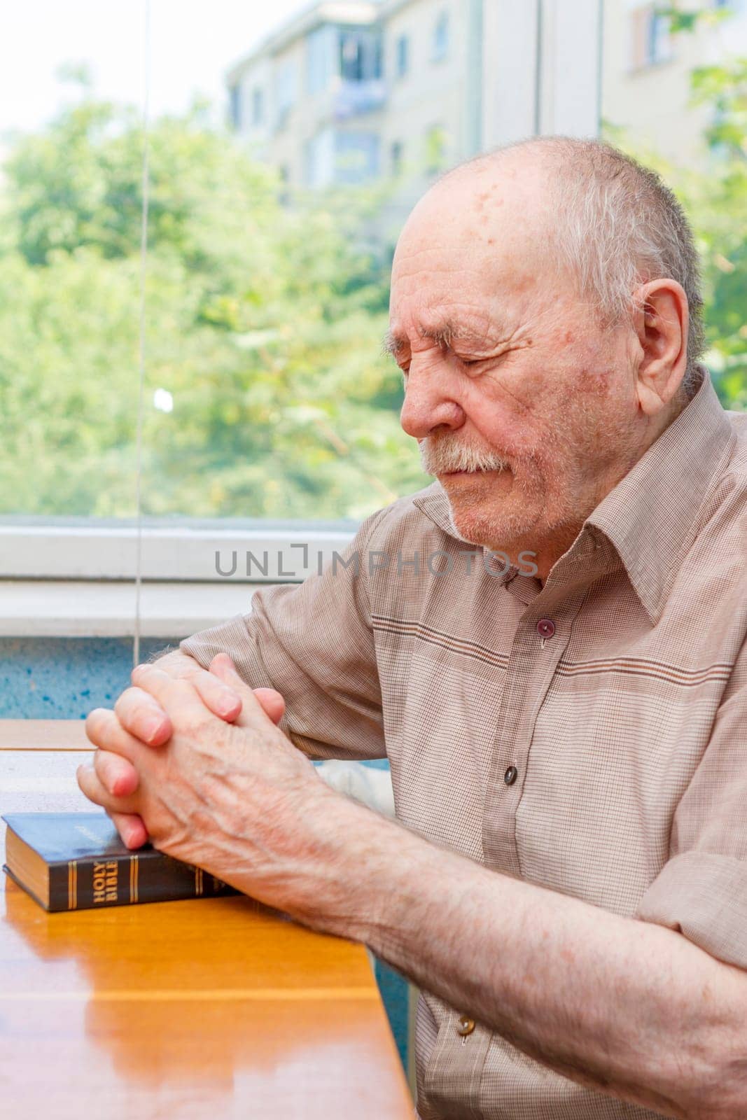 Old man praying at home near the window