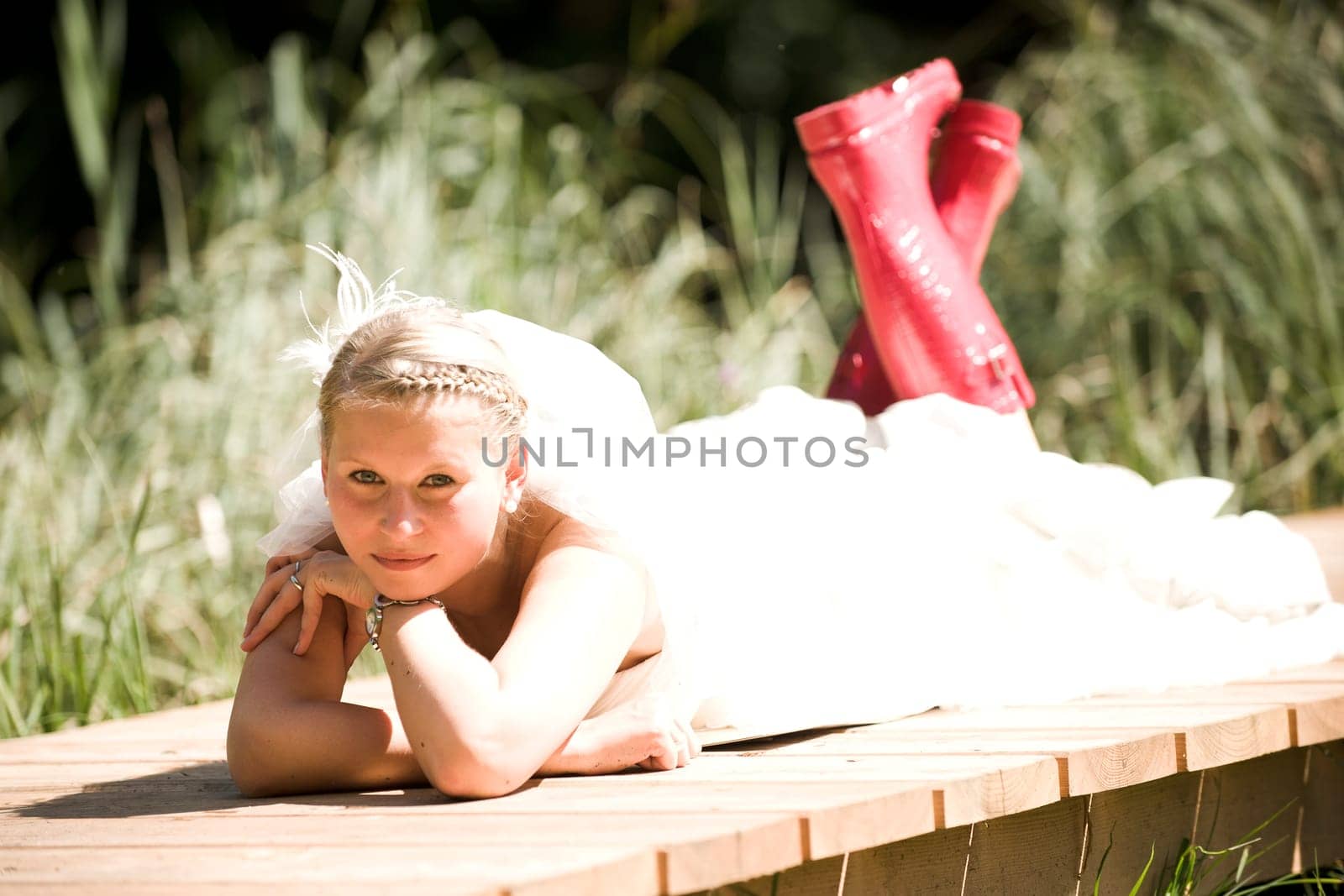 Bride with wedding dress and red rubber boots in nature