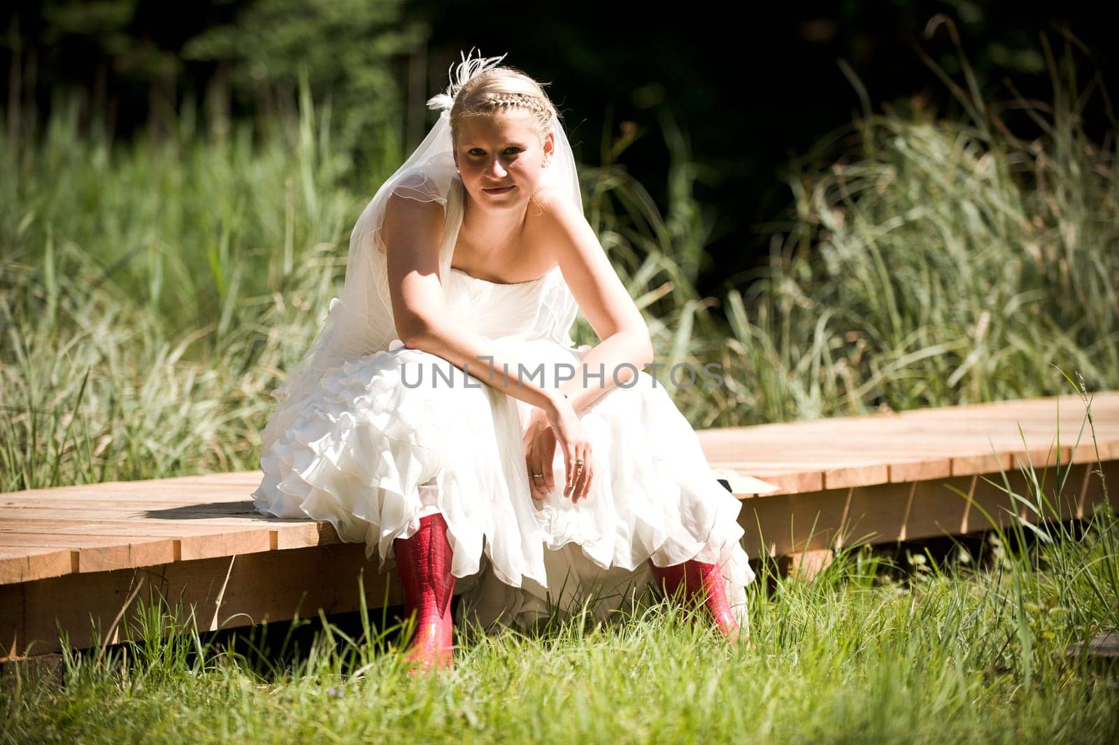 Bride with wedding dress and red rubber boots in nature