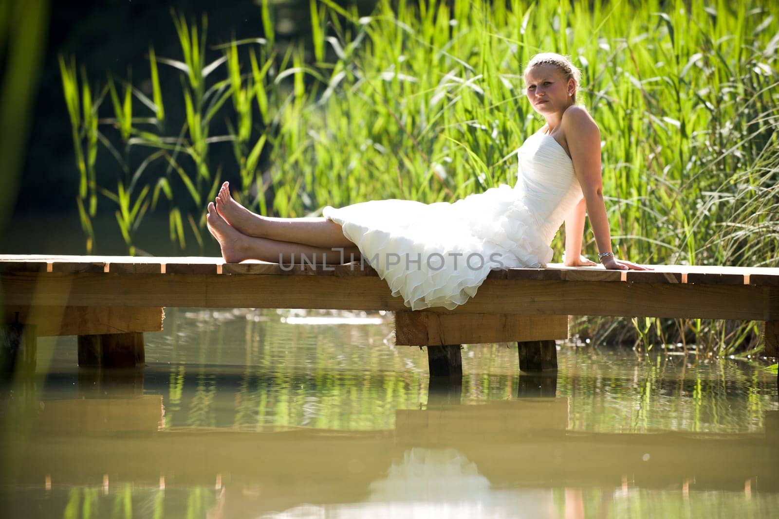 Bride in white wedding dress sitting lonely by a lake