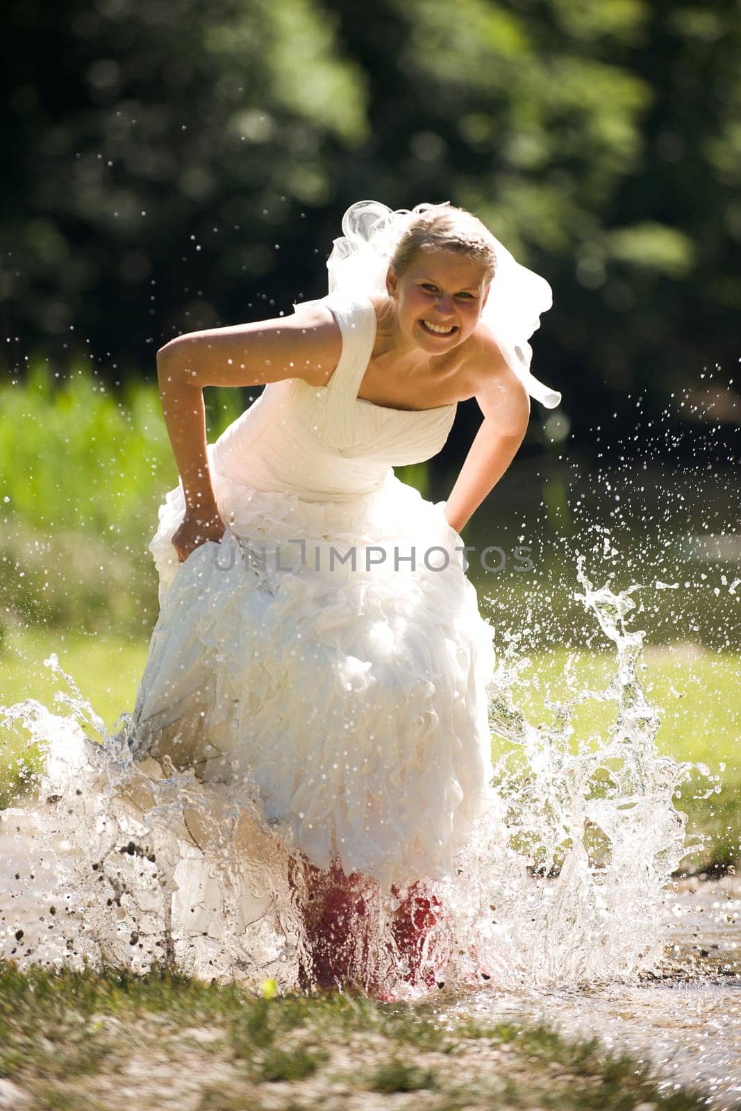 Bride splashes herself wet in small creek with red rubber boots