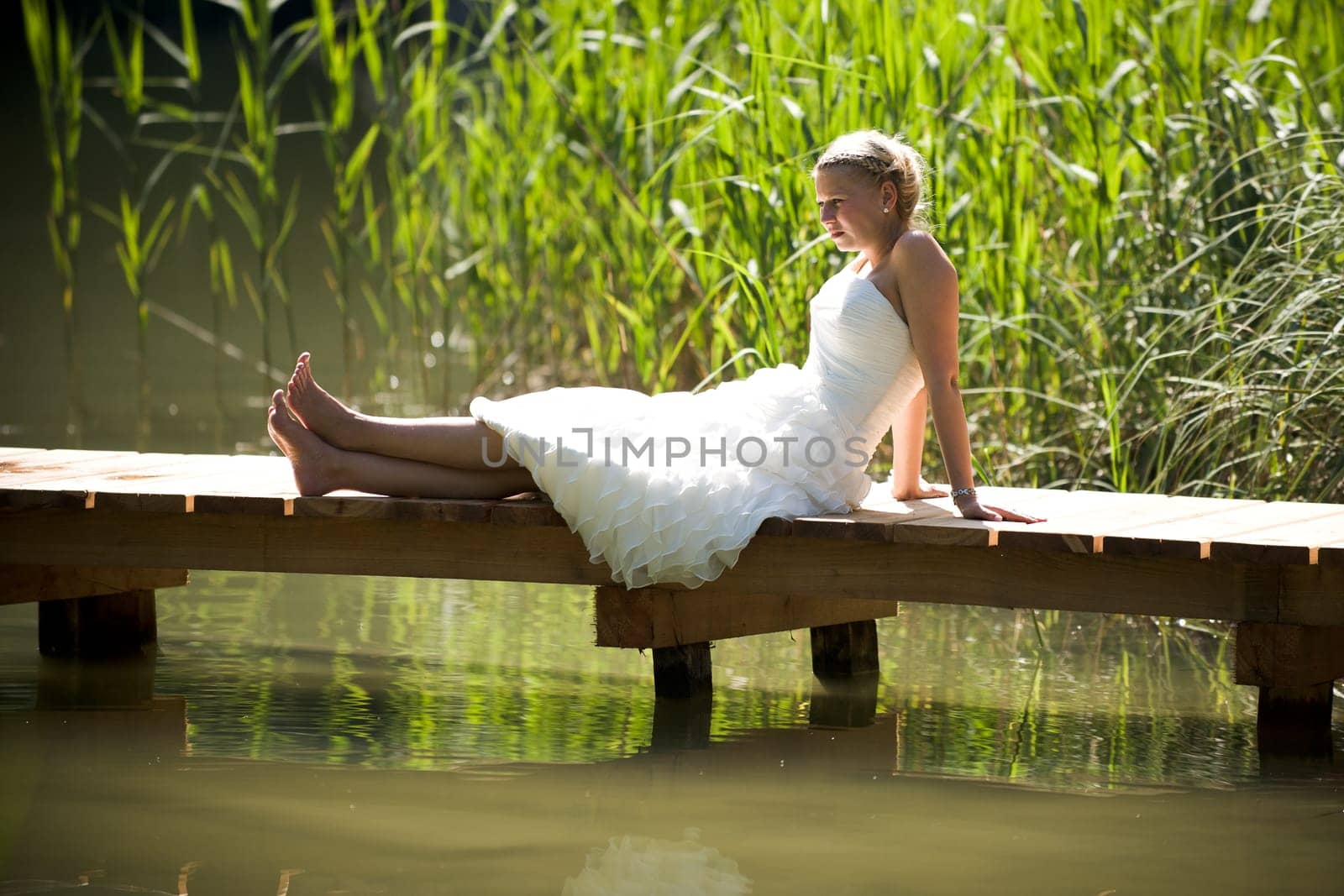 Bride in white wedding dress sitting lonely by a lake