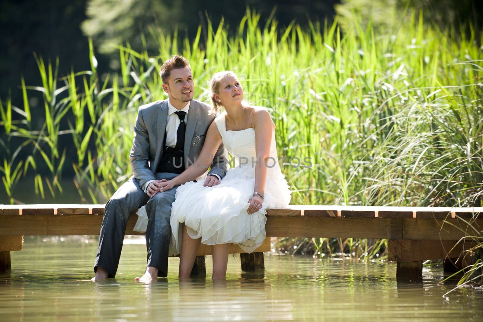 Bride and groom sitting romantically by a lake