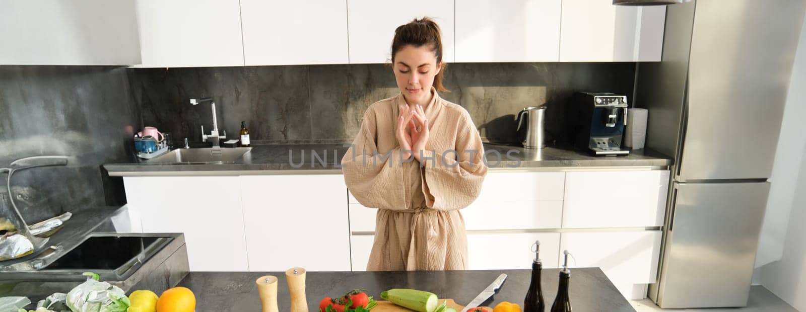 Portrait of excited woman looks thoughtful at chopping board with zucchini, vegetables, preparing healthy salad, making vegetarian meal, choosing what to have for dinner, standing in kitchen by Benzoix