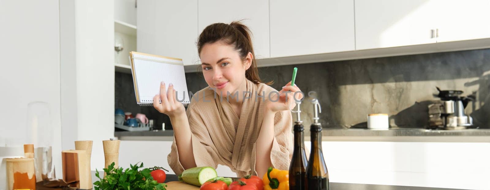 Portrait of woman cooking in the kitchen, reading her notes, checking recipe while preparing meal, making breakfast salad, writing down grocery list.